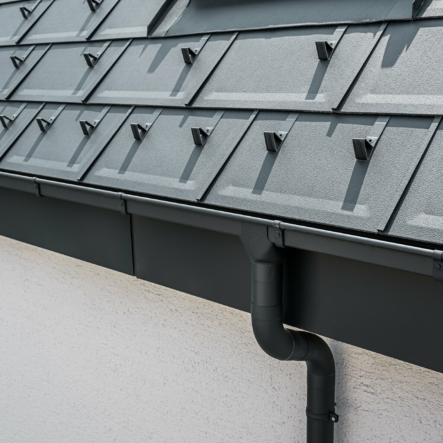 Steil dakoppervlak bedekt met de dakpan R.16 met vierkante PREFA bakgoot met trechteruitloop en afvoerbuis in antraciet