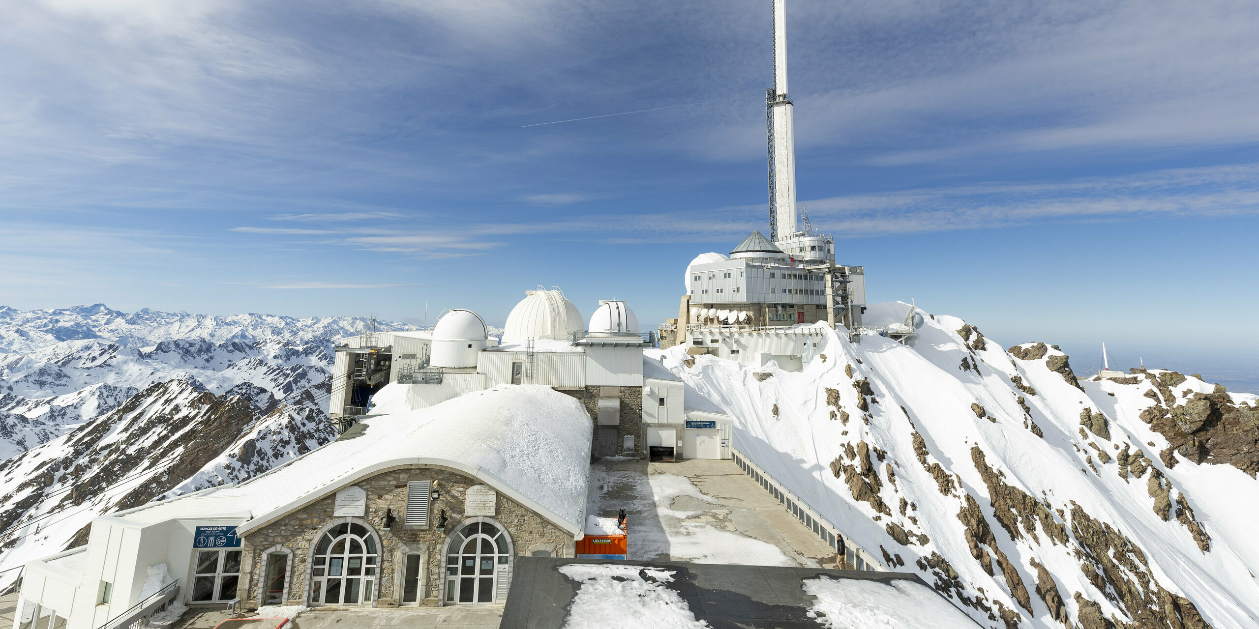Das Midi-Pyrénées-Observatorium, auf einem schneebedeckten Berggipfel gelegen, präsentiert seine umfassend sanierte und erweiterte Struktur. Die Fassade wurde mit PREFALZ in der Farbe P.10 Reinweiß gestaltet, optimal für die extremen Hochgebirgsbedingungen. Das Bild zeigt mehrere Kuppeln und das Hauptgebäude, das sich majestätisch gegen den blauen Himmel und die schneebedeckten Pyrenäen erhebt. Die Wetterbeständigkeit, Korrosionsbeständigkeit und Wartungsarmut von dem leichten Aluminium, das per Hubschrauber transportiert wurde, machten es zur perfekten Wahl. Die Bauarbeiten dauerten über drei Jahre, da sie nur in den Sommermonaten durchgeführt werden konnten.
