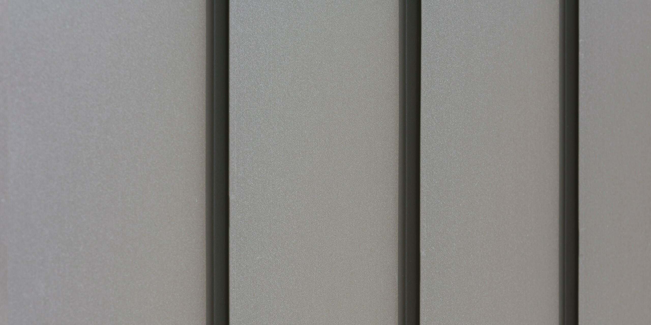 Gros plan d'un revêtement de façade moderne en aluminium avec des bacs verticaux créant un motif esthétiquement texturé. L'aluminium provient de PREFA Aluminium Products GmbH.