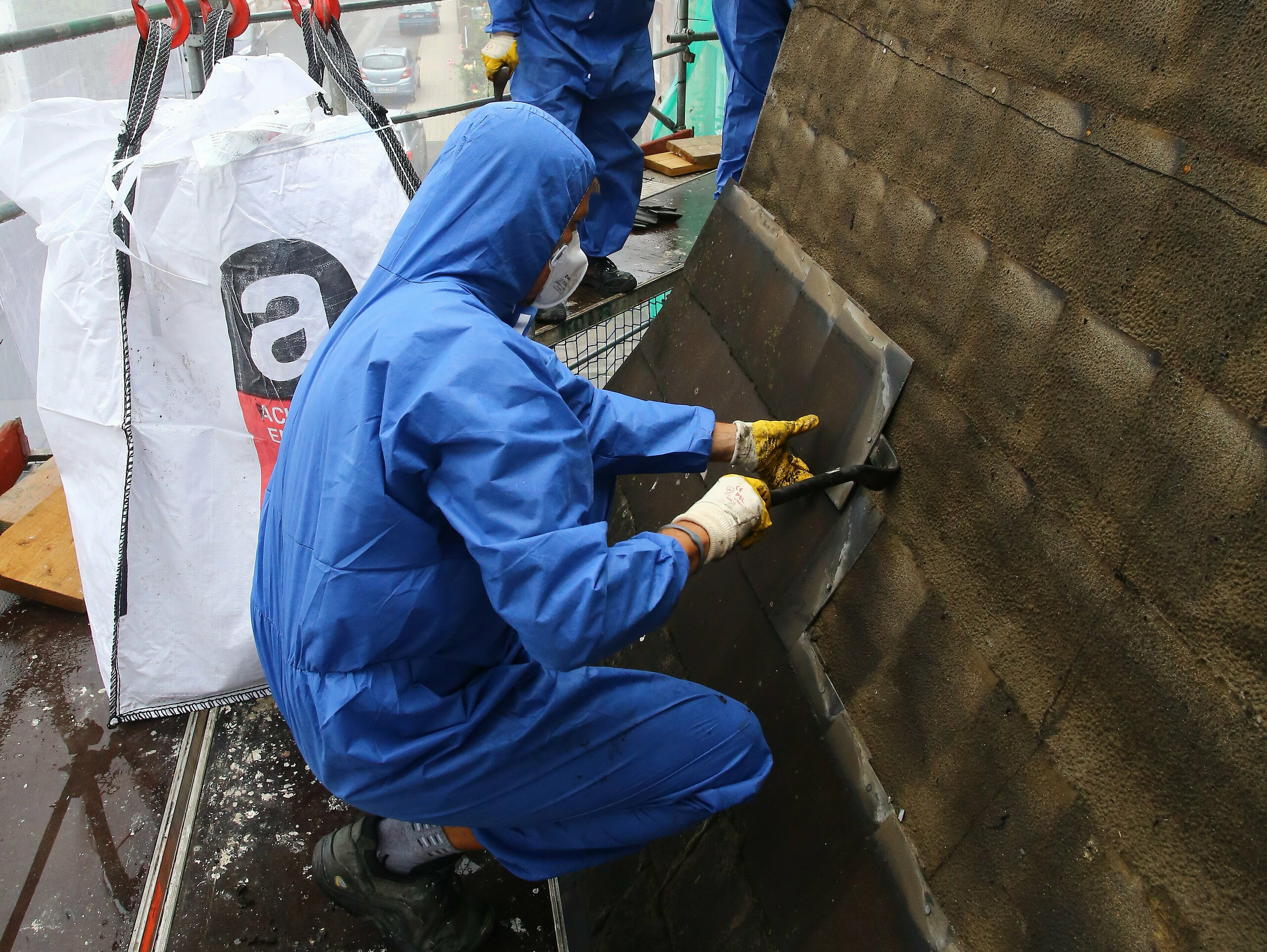 Geschulter Arbeiter beim Entfernen und Entsorgen der asbesthältigen, alten Dacheindeckung mit Mundschutz, um ein Einatmen des Asbests zu vermeiden