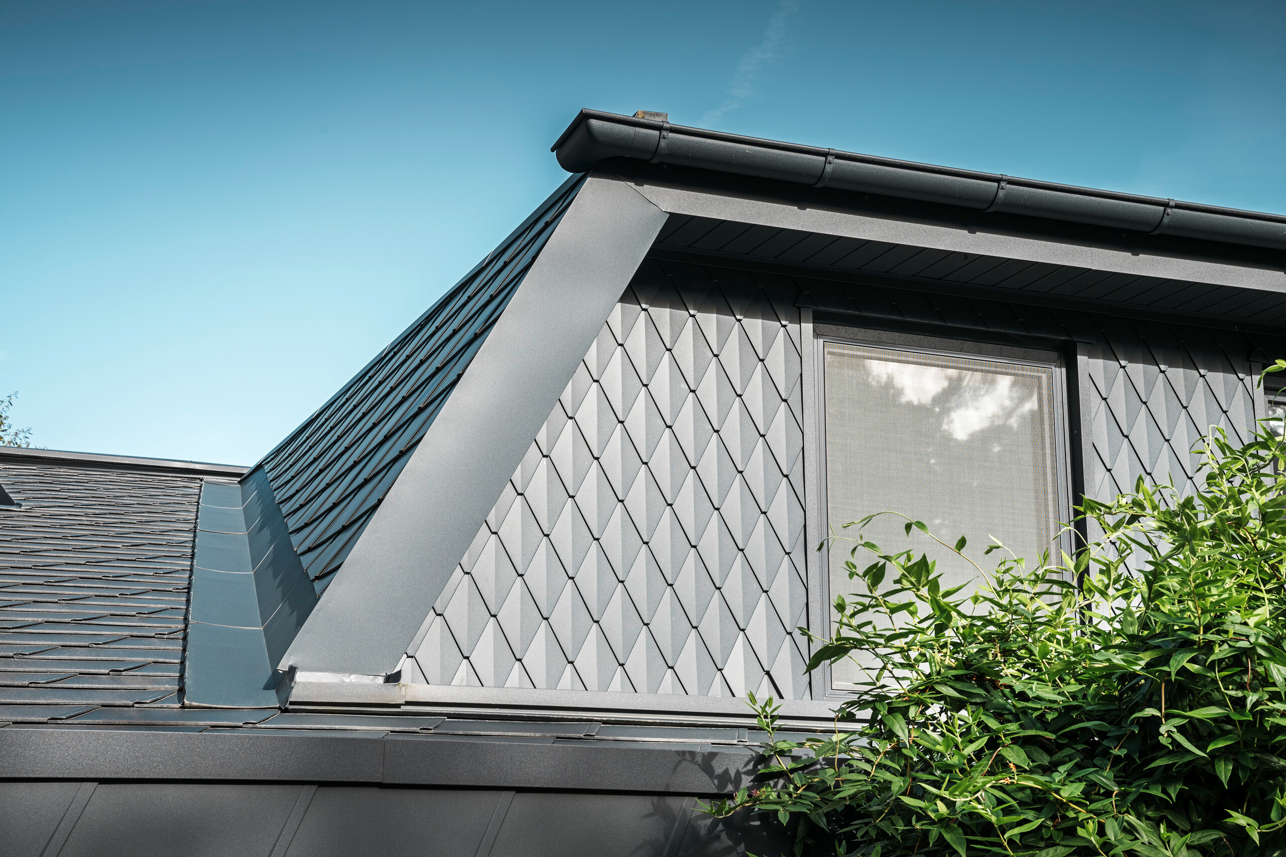 Lucarne trapézoïdale d'une maison individuelle à Mechernich, revêtue de petits losanges PREFA en P.10 anthracite. La toiture est recouverte de DS.19 PREFA de la même couleur. Le revêtement en aluminium de haute qualité garantit une résistance aux intempéries et un aspect moderne et esthétique.