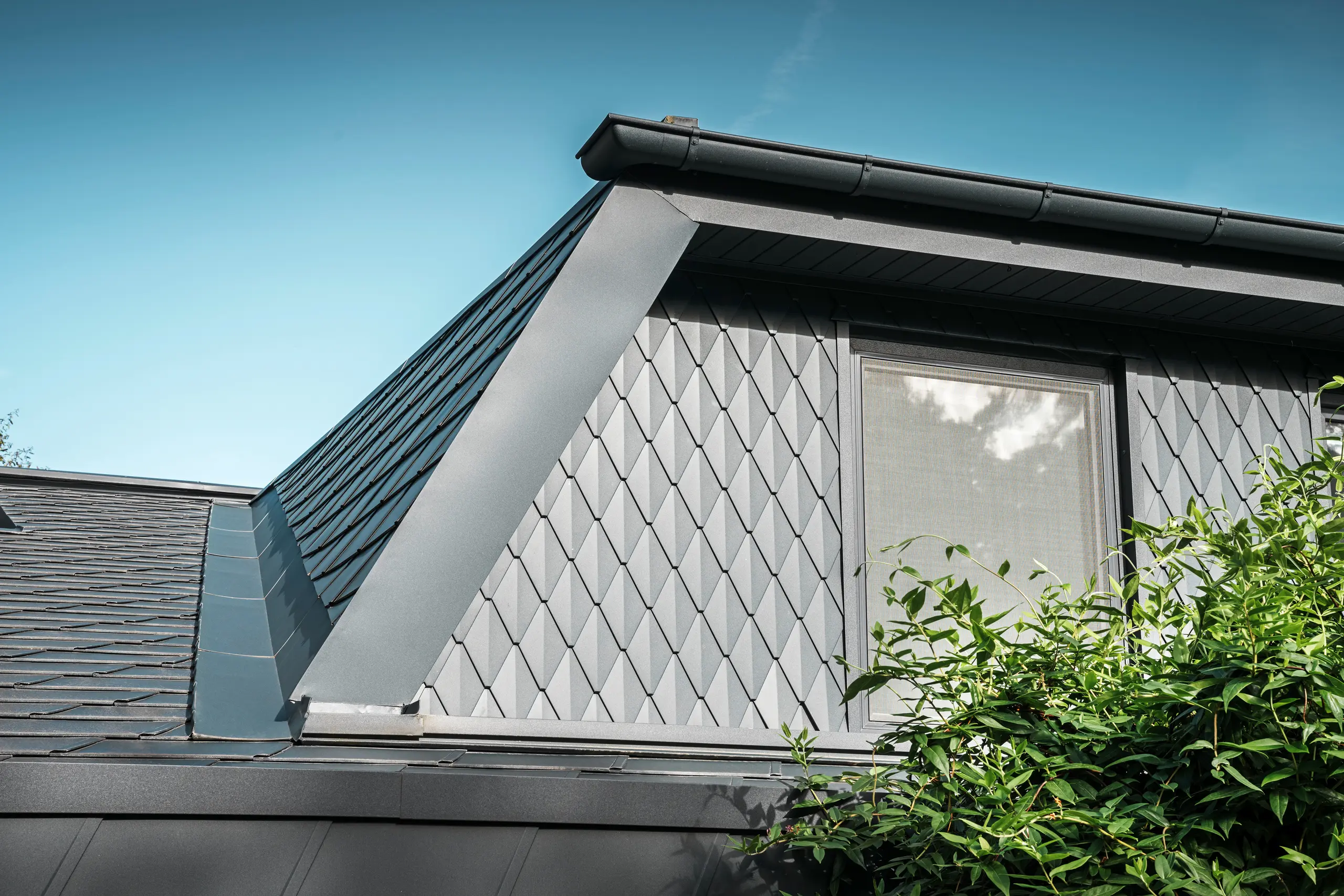 Trapeziumvormige dakkapel van een eengezinswoning in Mechernich, bekleed met kleine PREFA daklosange in P.10 antraciet. Het dak is bedekt met PREFA dakschindels DS.19 in dezelfde kleur. De hoogwaardige aluminium bekleding zorgt voor weerbestendigheid en een moderne, esthetische uitstraling.