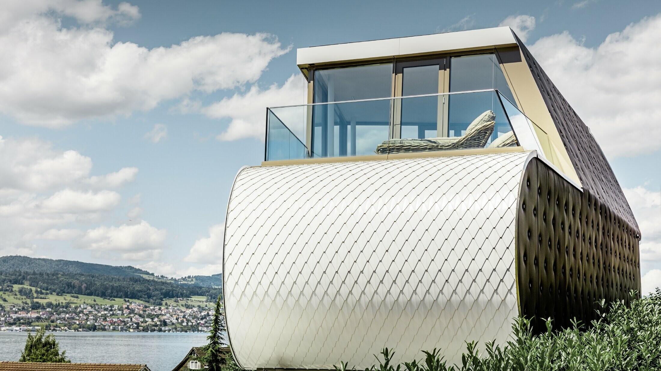 Vue latérale de la remarquable Flexhouse, conçue par l’architecte Camenzind. On voit l’un des murs extérieurs incurvés, revêtu de la façade en aluminium en écailles de PREFA, couleur blanc pur.