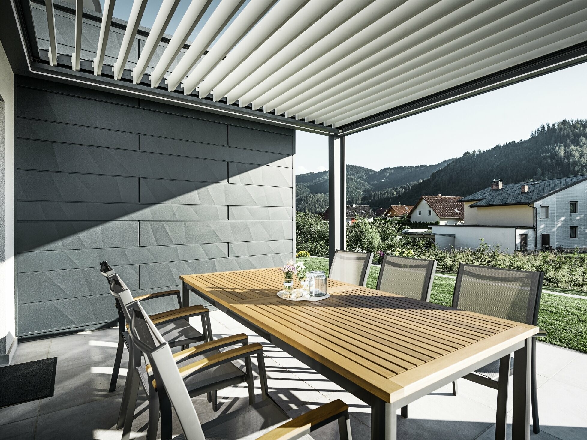 Met lamellen overdekt, beschut terras met tafel en stoelen, een gevelkant is bekleed met de PREFA Siding.X gevelpanelen in antraciet.