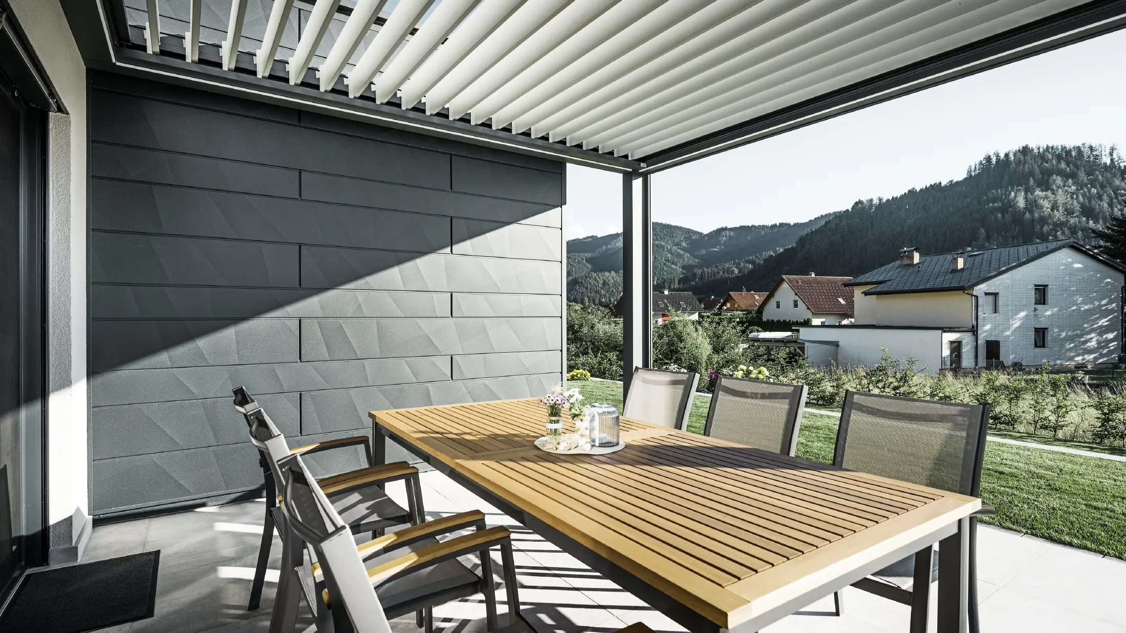 Terrasses couvertes de lamelles, protégées, avec table et fauteuils ; une façade est revêtue de panneaux de façade PREFA Siding.X anthracite.