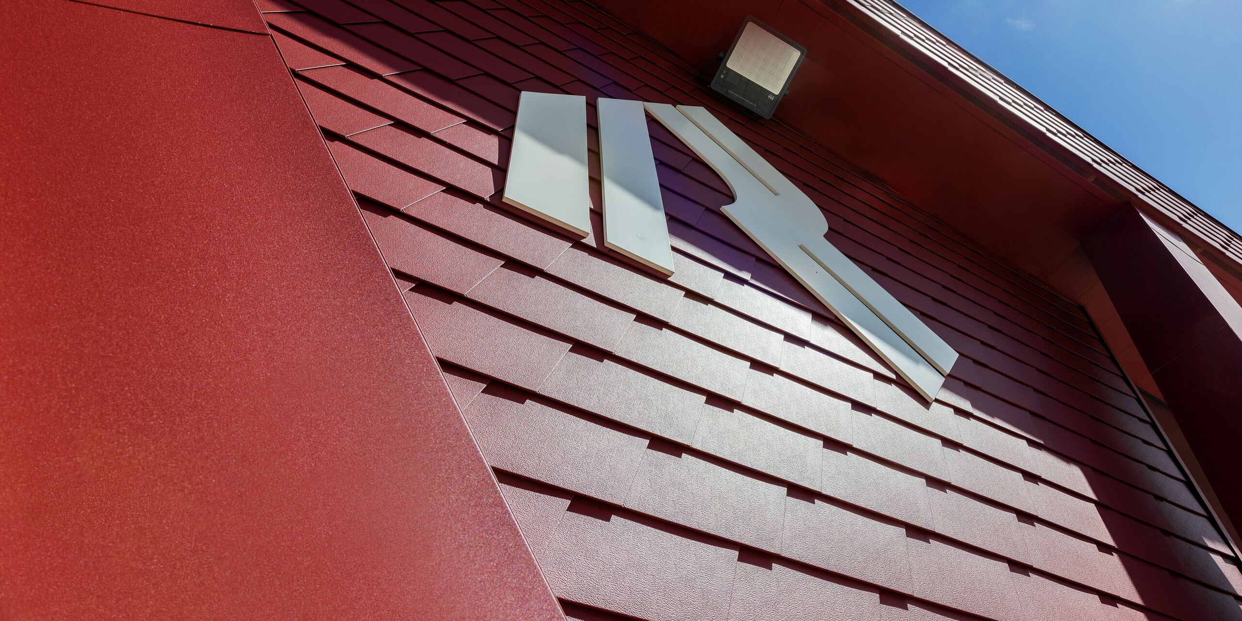 Die auffällige Fassade des Summit Mountain Clubs in Ratschings zeigt das markante P.10 Oxydrot-Design mit den präzise verlegten PREFA Wandschindeln und dem auffälligen Logo des Bergrestaurants, der auch als Eventlocation dient. Die robuste Aluminiumverkleidung bietet sowohl ästhetische Highlights als auch hervorragenden Schutz vor den extremen Wetterbedingungen der Berge. Das moderne Design harmoniert perfekt mit der alpinen Umgebung und sorgt für einen bleibenden Eindruck.