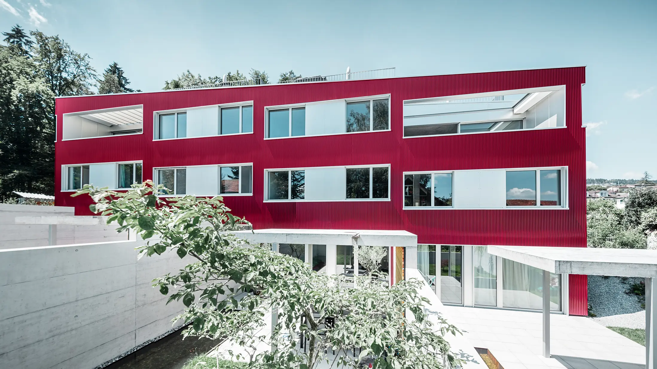 Wohnhausanlage mit Flachdach und Balkonen mit weinroter Fassade mit PREFA Welle