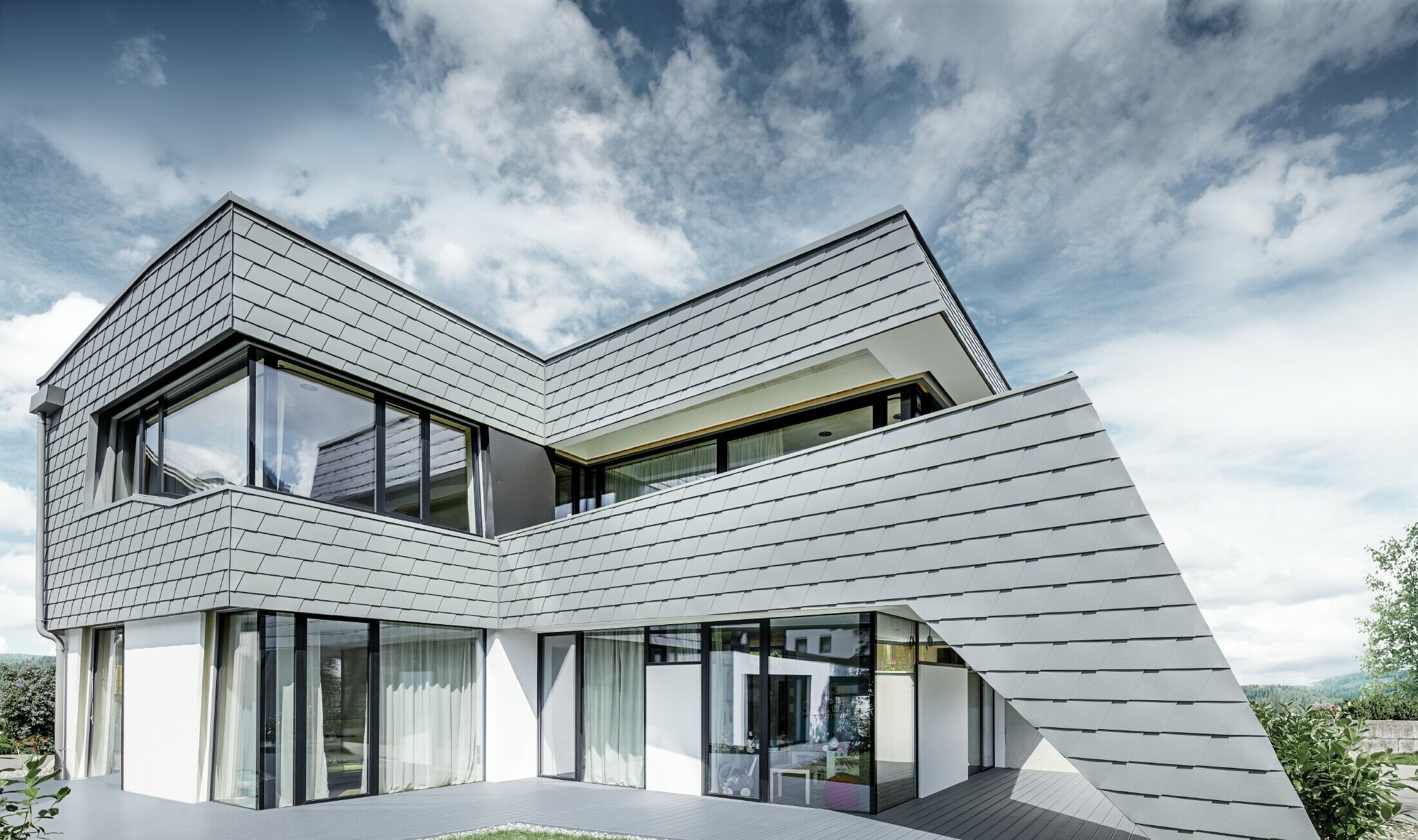 Moderne gezinswoning met plat dak, grote raamoppervlakken en aluminiumgevel met lichtgrijze schindels van PREFA