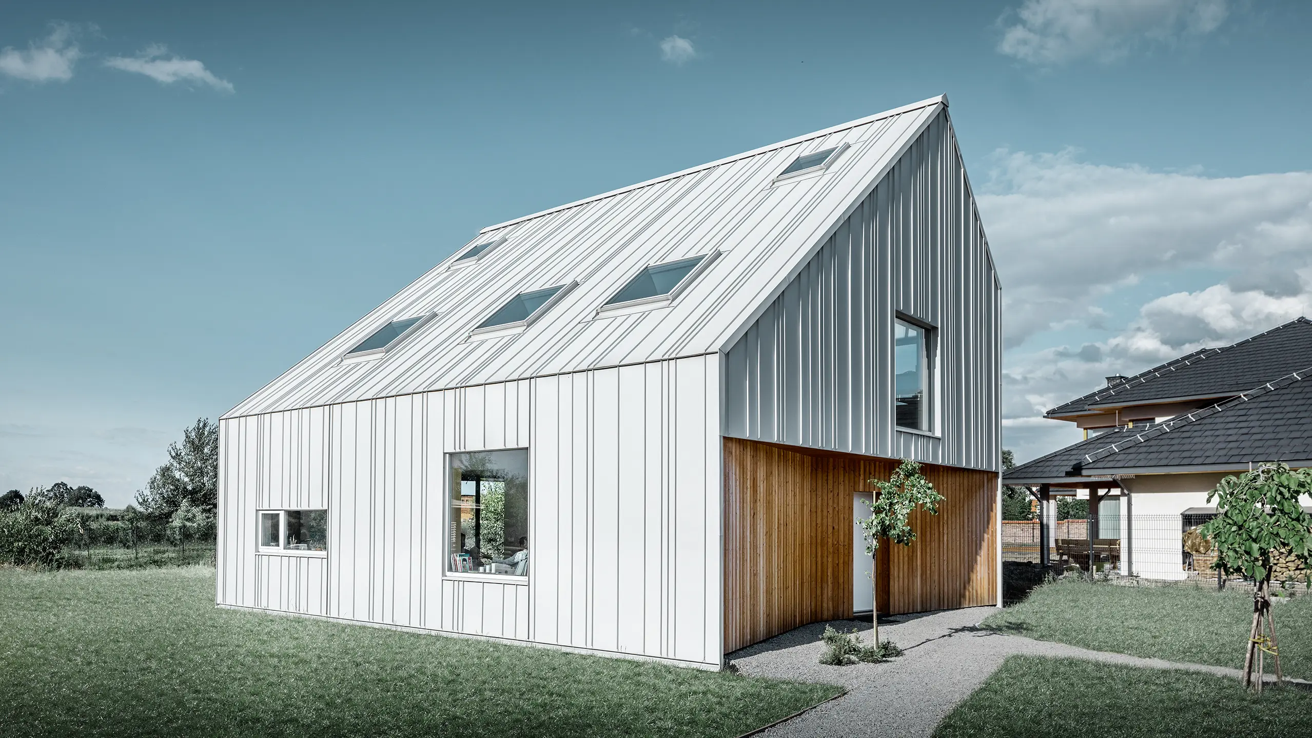 Modern vormgegeven eengezinswoning met zadeldak, de volledige buitenkant is bekleed met PREFALZ in prefawit. Daarbij lopen de verschillend brede panelen van het dak door over de gevel. In het dak bevinden zich verschillende dakvensters.