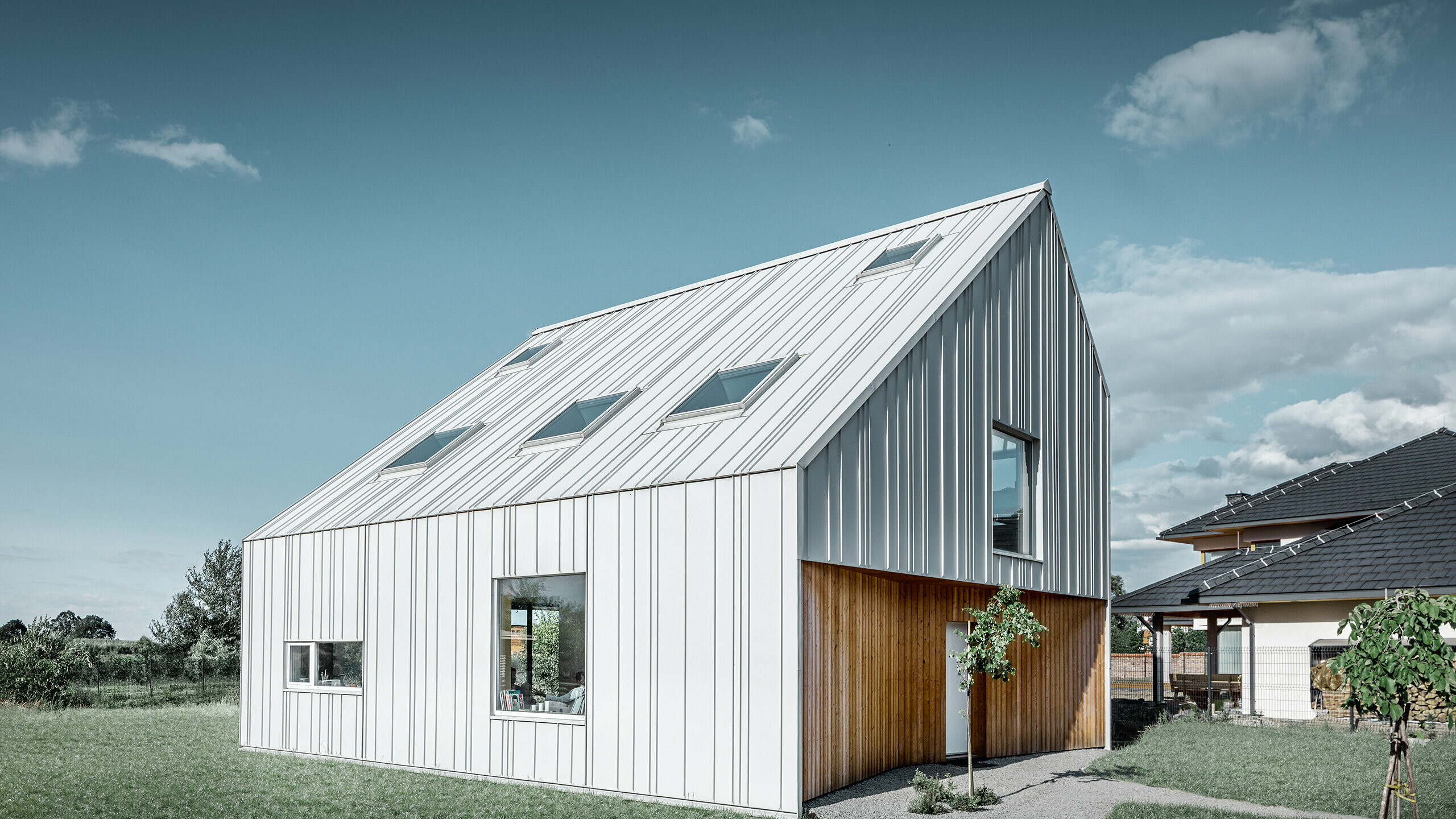 Modern vormgegeven eengezinswoning met zadeldak, de volledige buitenkant is bekleed met PREFALZ in prefawit. Daarbij lopen de verschillend brede panelen van het dak door over de gevel. In het dak bevinden zich verschillende dakvensters.