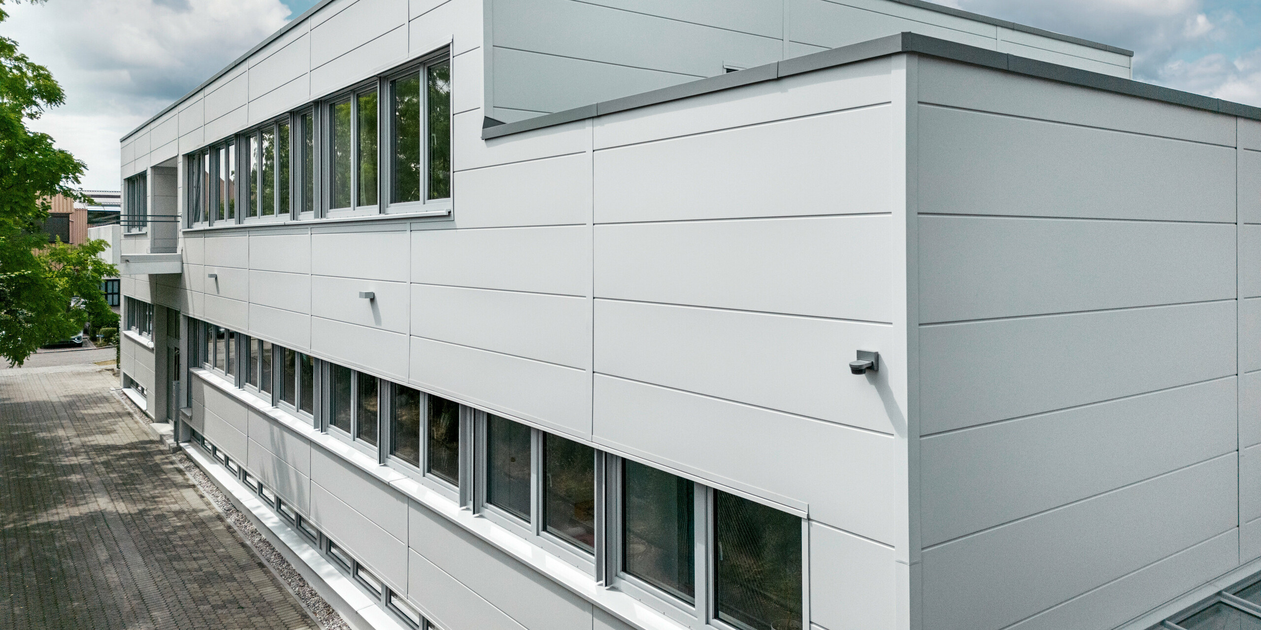 Des Sidings PREFA grand format entourent un bâtiment d'entreprise à Oberschleißheim (Allemagne). Les éléments de façade extra-larges en aluminium ont été choisis dans la couleur blanc Prefa.