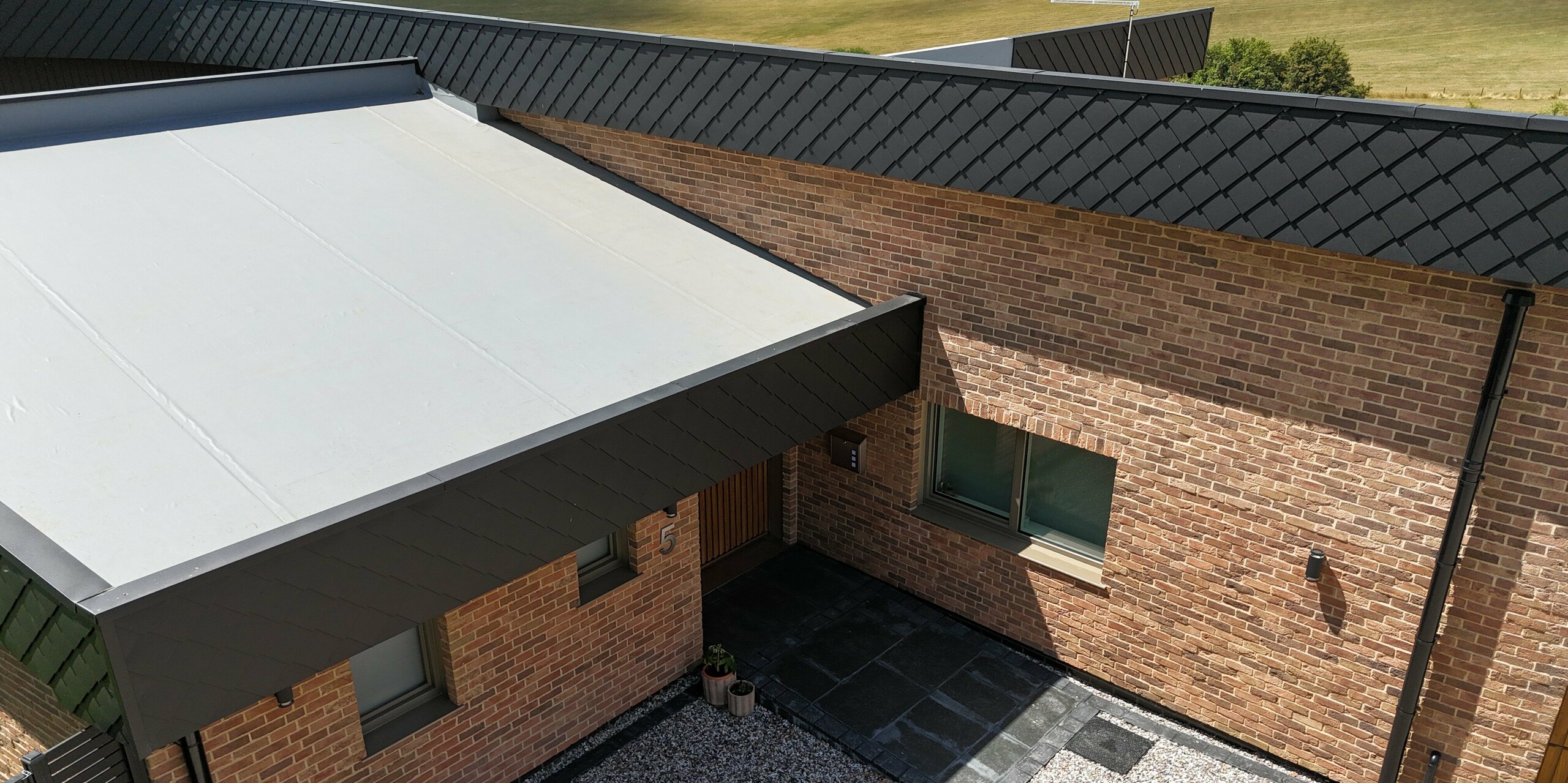 Dieses moderne Einfamilienhaus besticht durch seine markante Eingangsüberdachung sowie die elegante Kombination aus Klinkerfassade und PREFA Wandraute 20 × 20 in Anthrazit. Die langlebigen Blechrauten setzen klare Akzente und unterstreichen die hochwertige Architektur. Dank der robusten PREFA-Aluminiumprodukte ist die Fassade witterungsbeständig und pflegeleicht. Die Verbindung natürlicher Materialien mit modernen Aluminiumlösungen macht dieses Objekt zu einem Eyecatcher für nachhaltiges und stilvolles Wohnen.