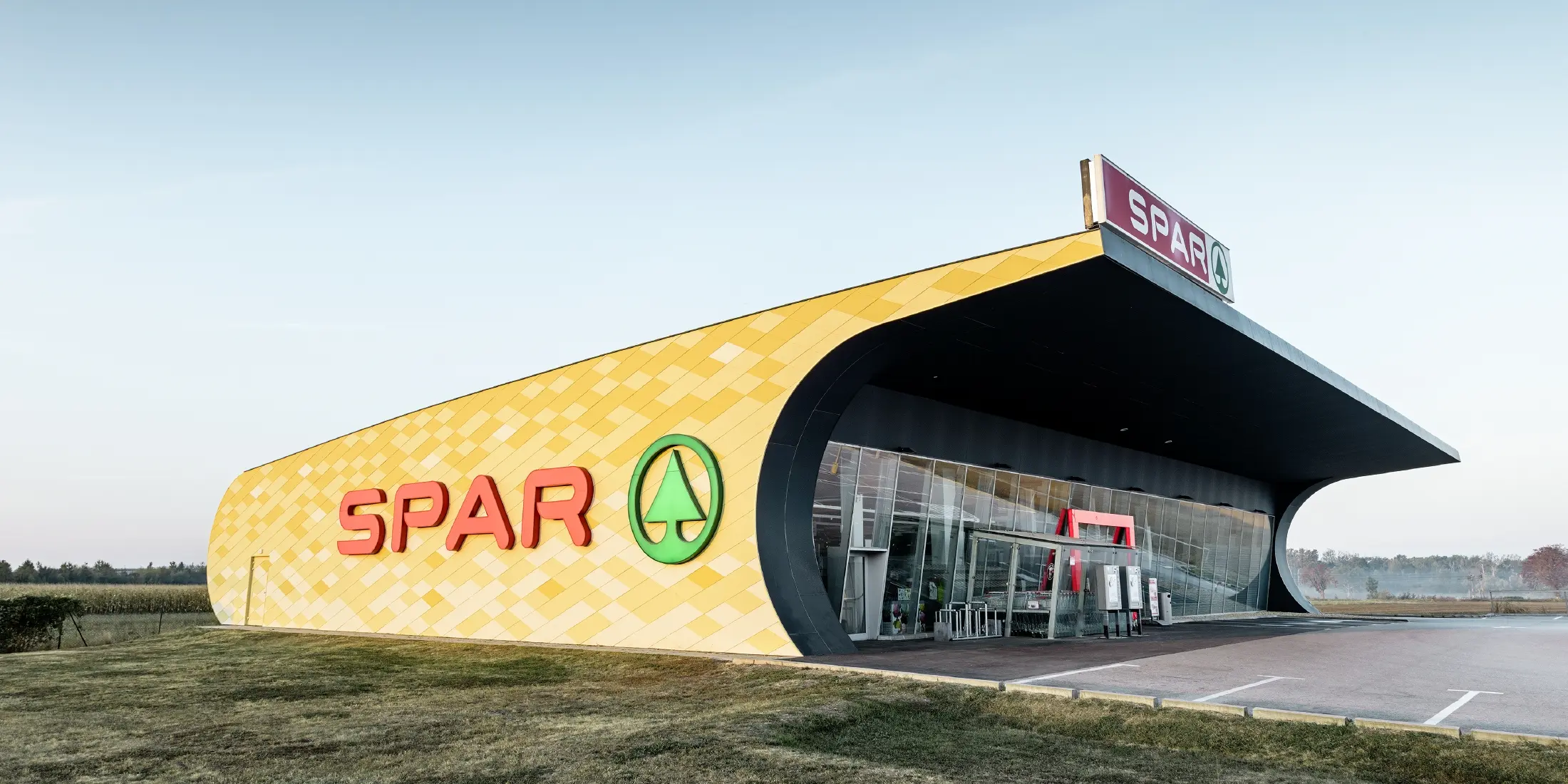 Spar Filiale mit einer Aluminiumfassade in gelb-orangen Karos und Spar Logo