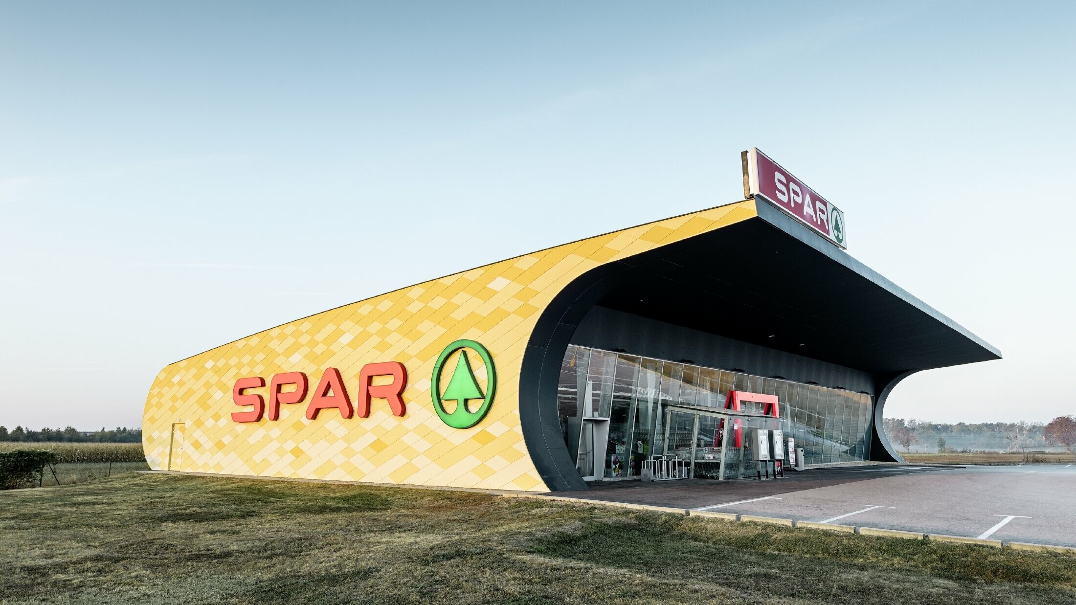 Spar Filiale mit einer Aluminiumfassade in gelb-orangen Karos und Spar Logo