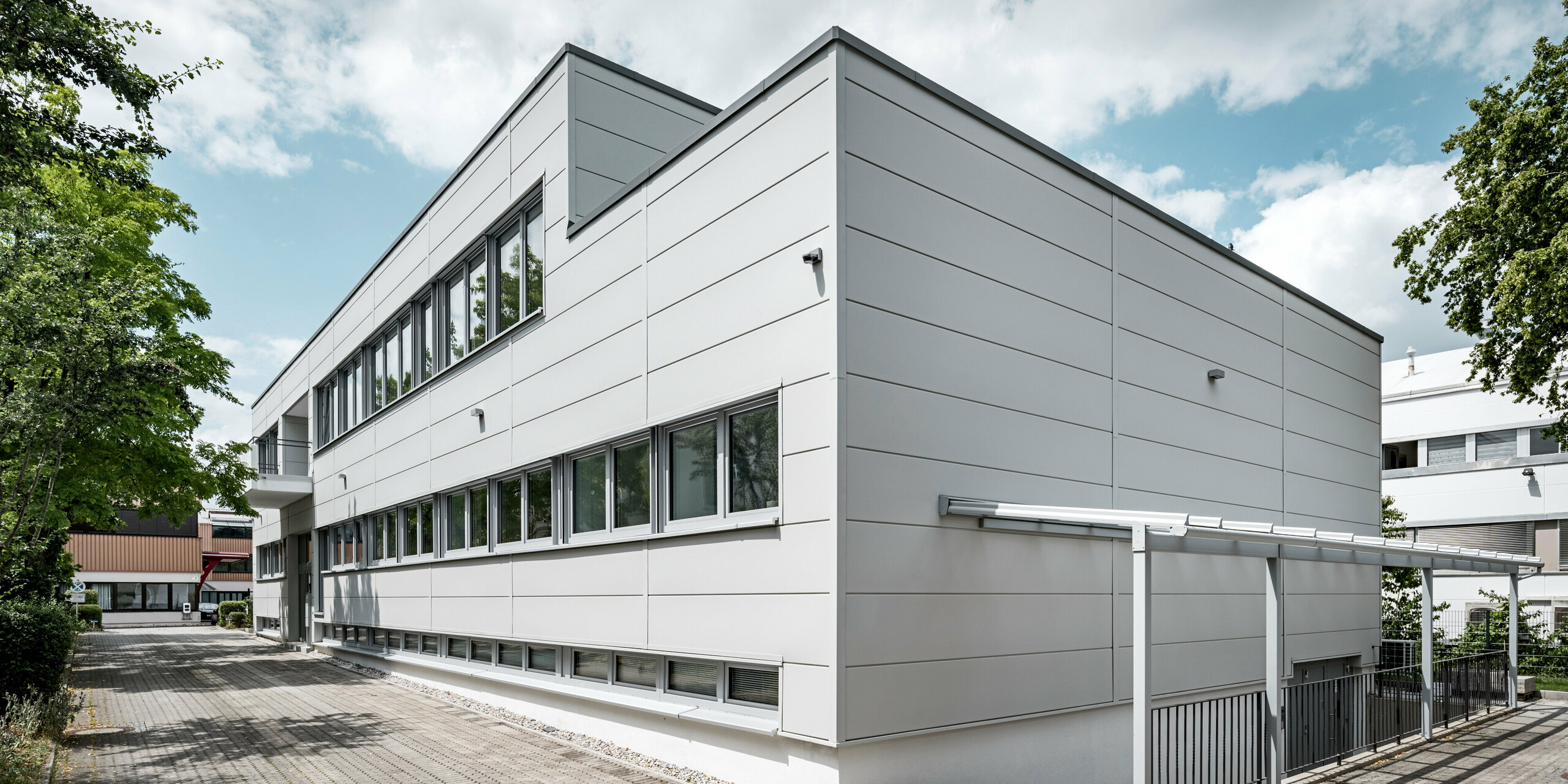 Des Sidings PREFA grand format entourent un bâtiment d'entreprise à Oberschleißheim (Allemagne). Les éléments de façade extra-larges en aluminium ont été choisis dans la couleur blanc Prefa.