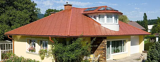 Bungalow mit gelber Fassade und der PREFA Dachschindel in Ziegelrot eingedeckt.