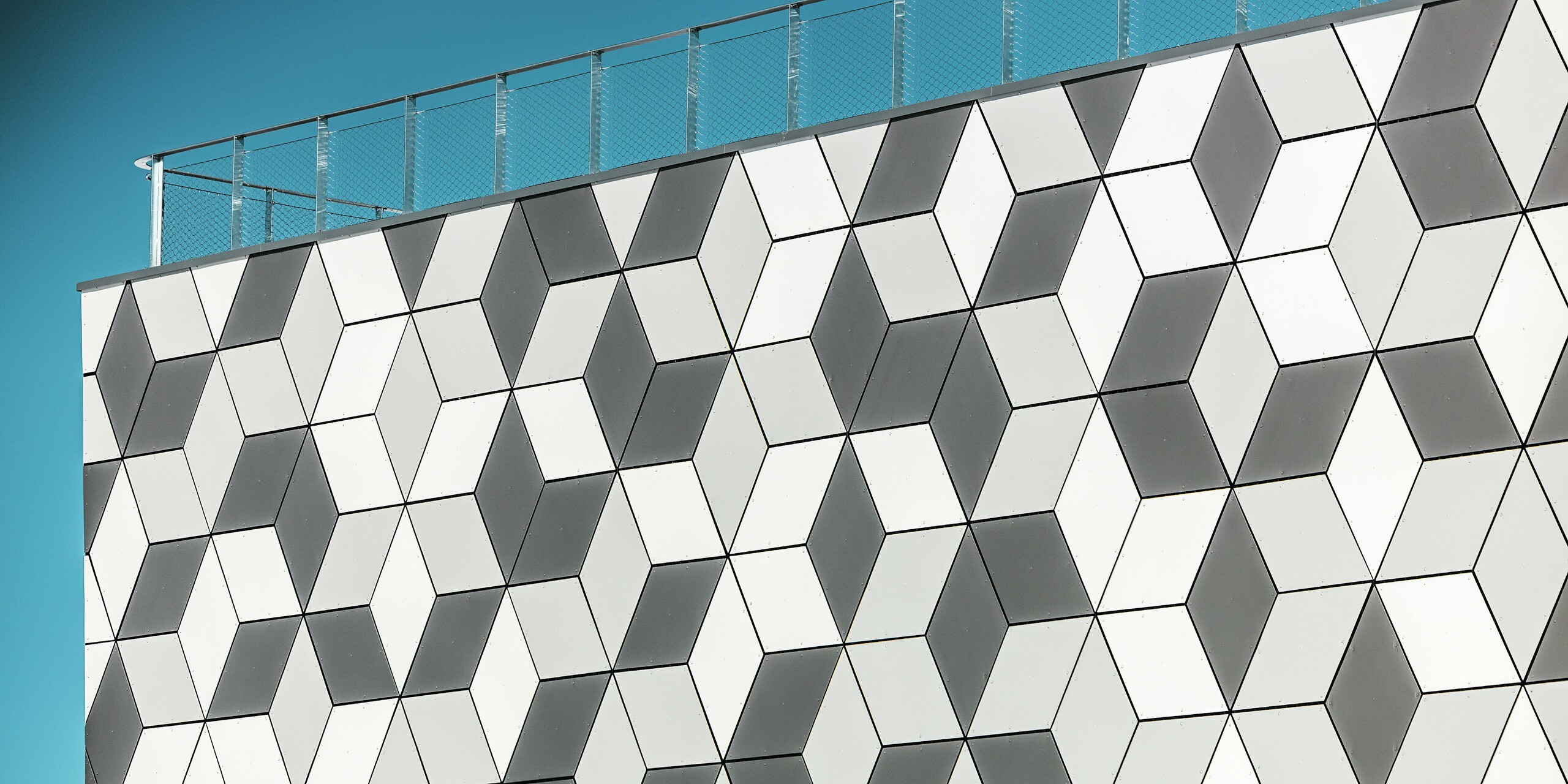 La façade de la station de téléphérique des Deux Alpes impressionne par son design dynamique et géométrique, réalisé avec des panneaux composites en aluminium PREFABOND en forme de losange. L'agencement précis des panneaux, déclinés dans différentes nuances de blanc et de gris, crée un effet 3D fascinant qui s'intègre parfaitement à l'architecture minimaliste. Grâce à la résistance au gel et à la durabilité des produits en aluminium PREFA, la façade conserve son esthétique et sa fonctionnalité, même dans des conditions climatiques extrêmes en montagne.