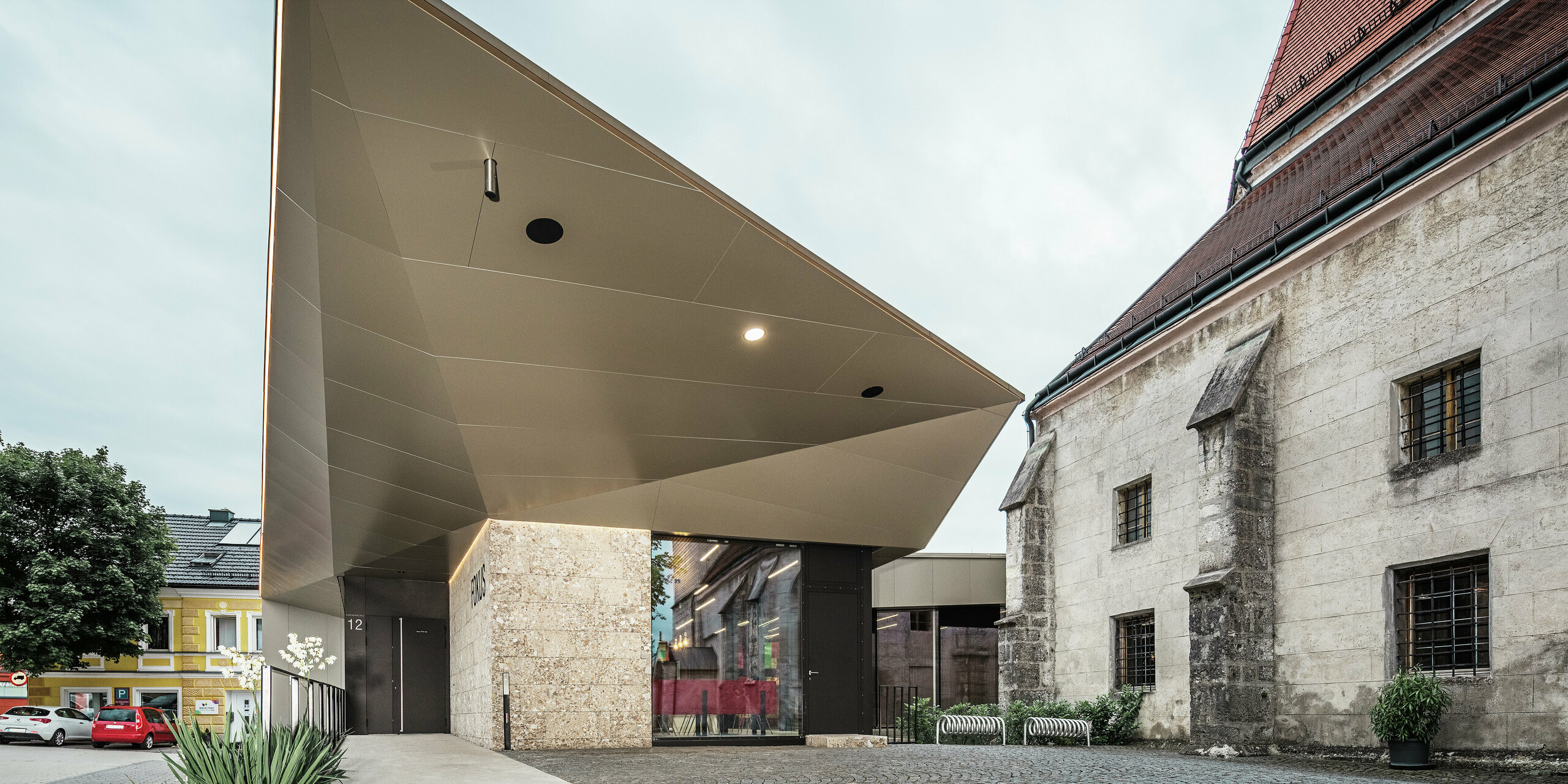 Ein Blick unter das kantig gefaltete Vordach offenbart die raffinierte Verarbeitung der bronzefarbenen PREFA Aluminium Verbundplatten. Diese bieten optimalen Korrosionsschutz, sind UV-beständig und verleihen der Konstruktion eine futuristische, fast schwerelose Ästhetik.