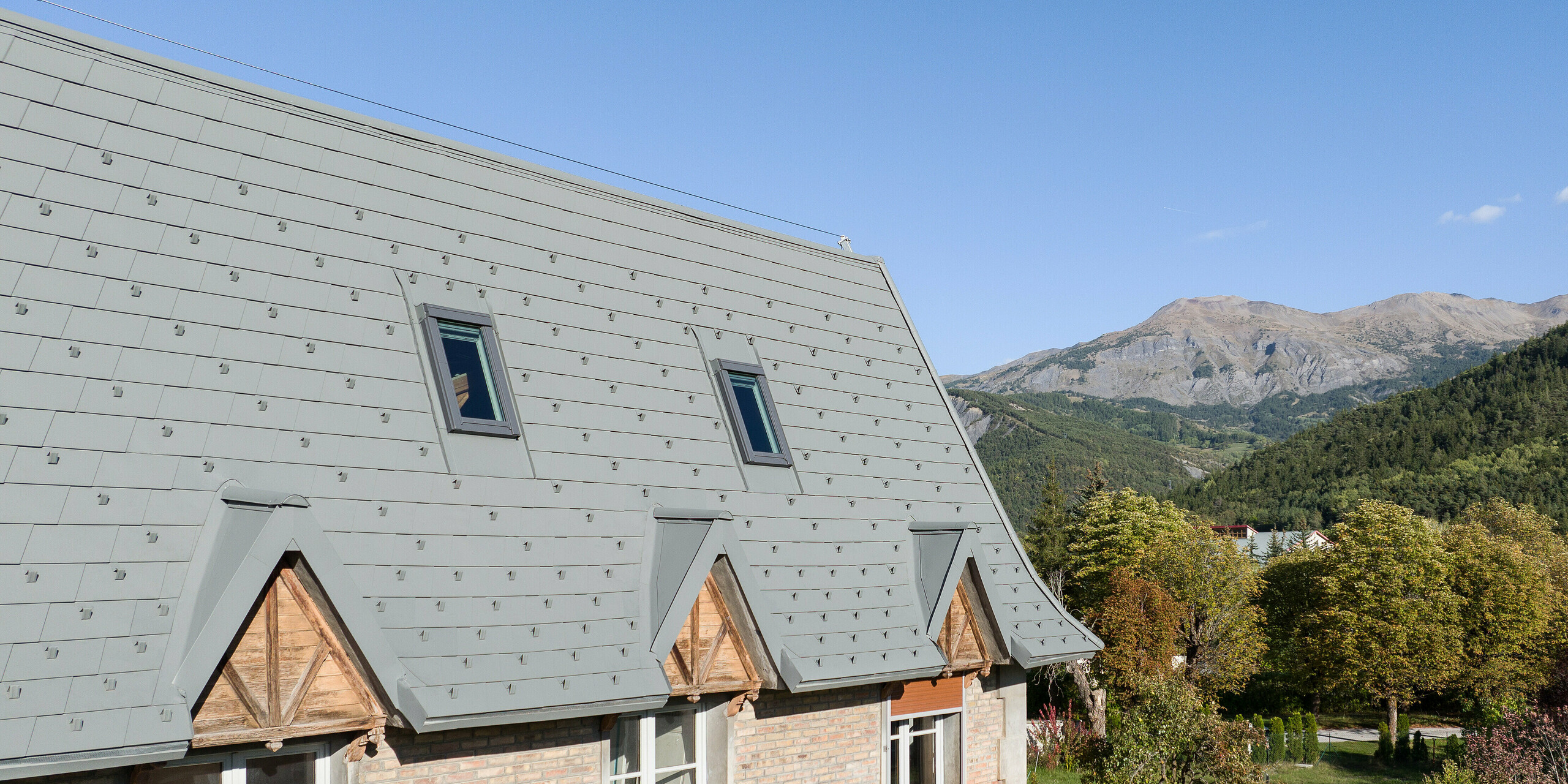 Die großflächige Dachlandschaft eines Anwesens in Barcelonnette, Frankreich wurde mit der PREFA Dachschindel in P.10 Hellgrau saniert. 