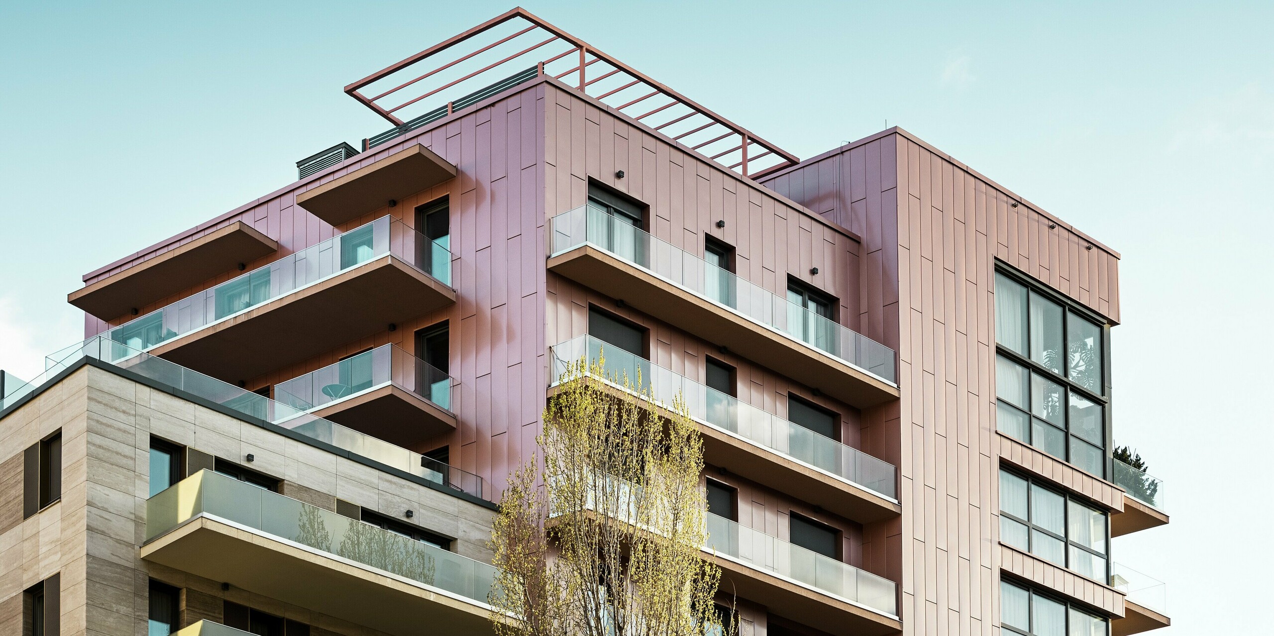 La partie supérieure du complexe résidentiel Grand Corvin présente de généreuses surfaces vitrées et des balcons modernes, encadrés par des panneaux de façade Siding PREFA, posés verticalement et déclinés dans une couleur saumon métallisée. Ce revêtement en aluminium, durable et résistant aux intempéries, souligne le concept architectural de matériaux de haute qualité et d'aménagement urbain au cœur de Budapest.