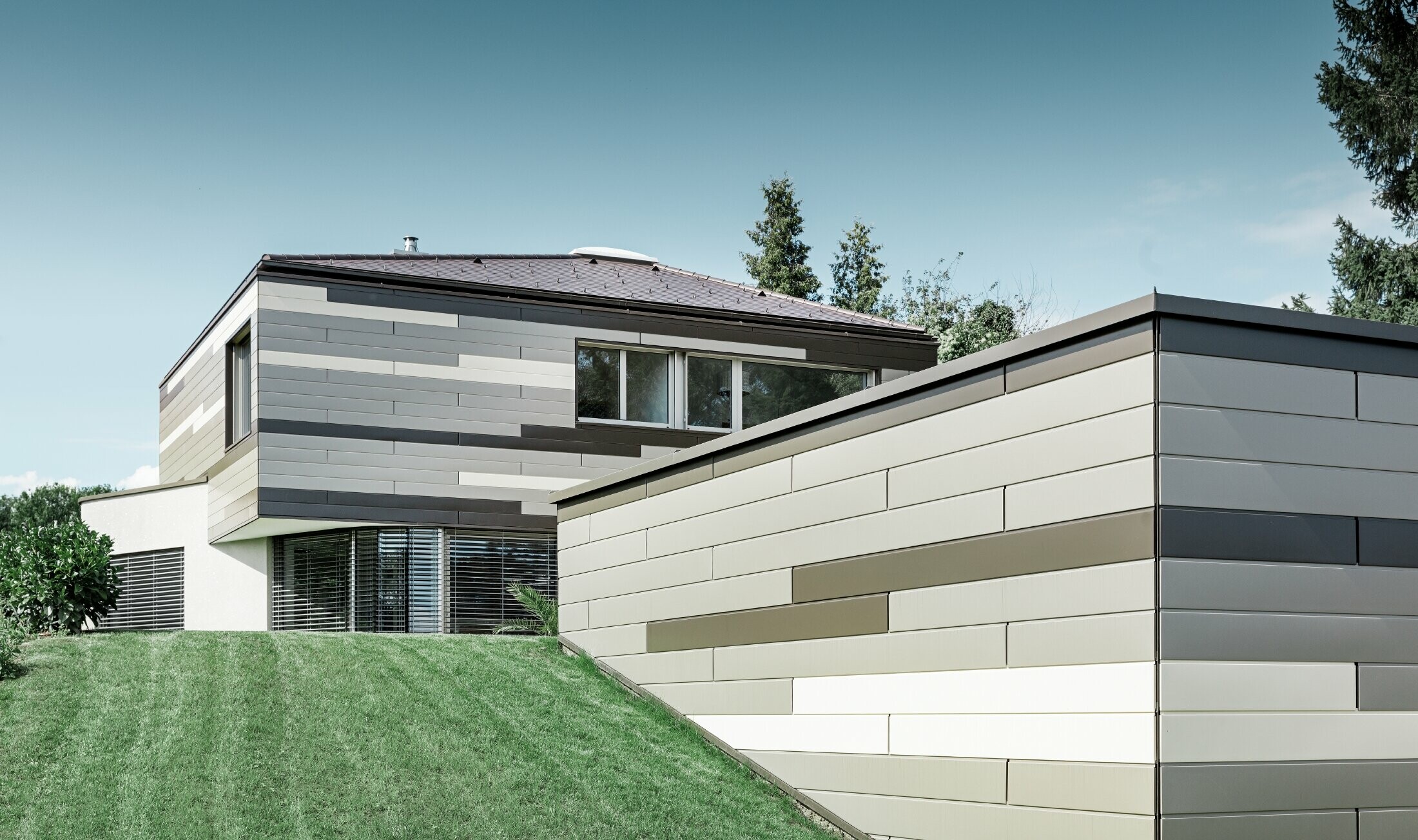 Modernes Einfamilienhaus mit Flachdach und überdachter Terrasse mit einer individuell gestalteten Aluminiumfassade aus Sidings in braun, bronze und elfenbein von PREFA