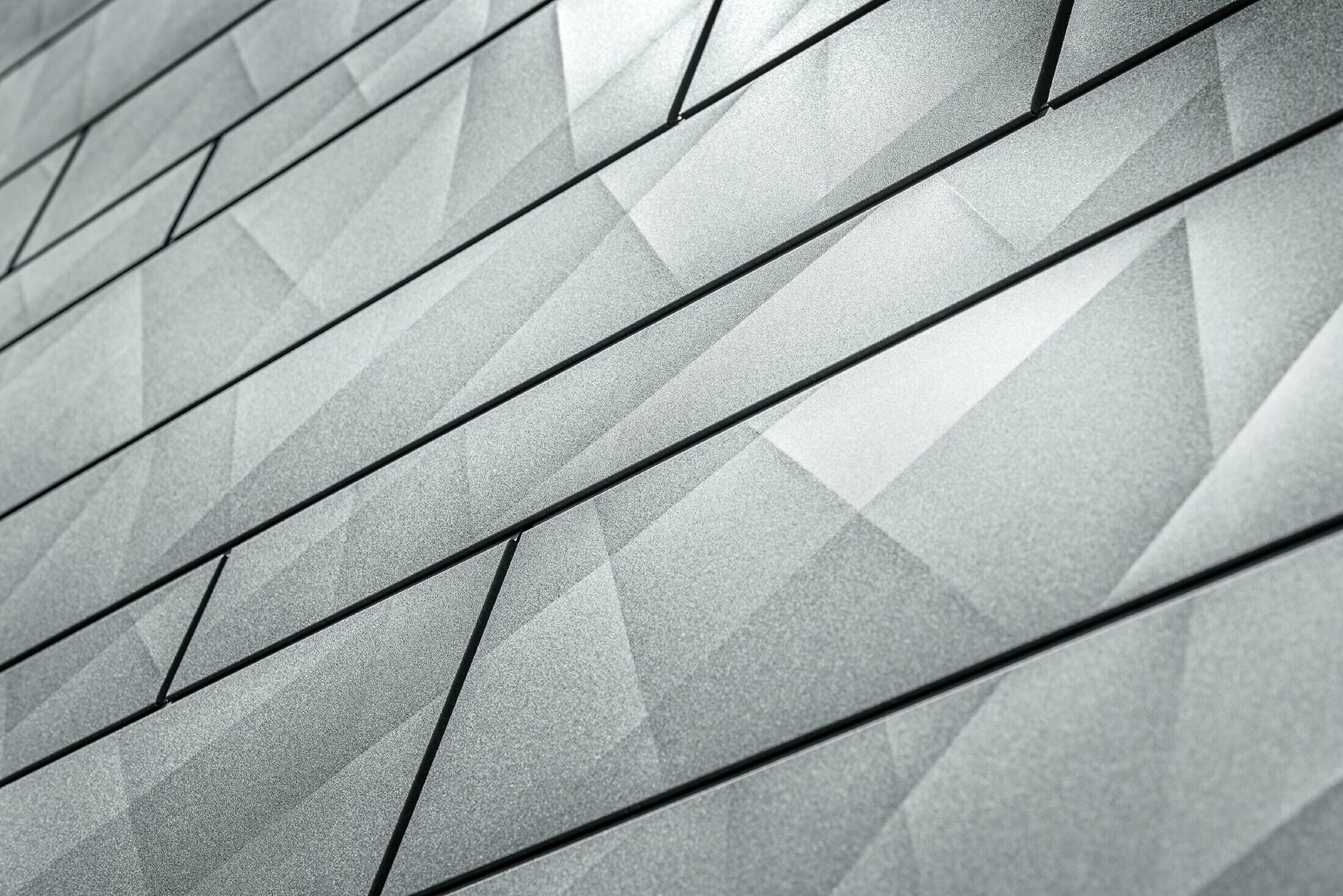 Gros plan sur le panneau de façade Siding.X couleur gris pierre de PREFA. Sur les panneaux, on aperçoit les plis irréguliers avec l’aspect naturel de l’imitation pierre.