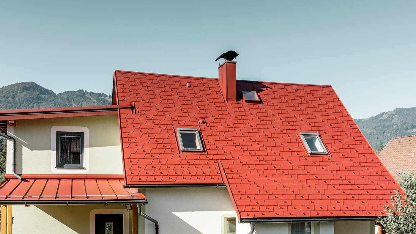 Klassisches Einfamilienhaus mit zwei Dachfenstern und Kamin, eingedeckt mit der neuen PREFA Dachschindel DS.19 in P.10 Oxydrot.