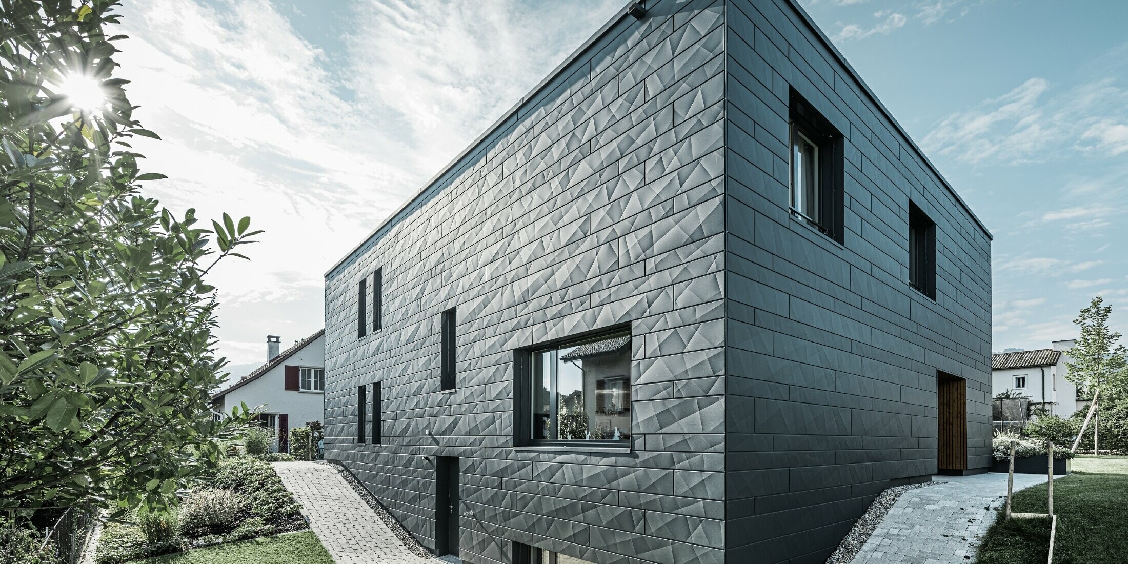 Photo latérale de la maison individuelle moderne prise depuis l’angle. Les rayons du soleil donnent à la façade en Siding.X un aspect très dynamique.