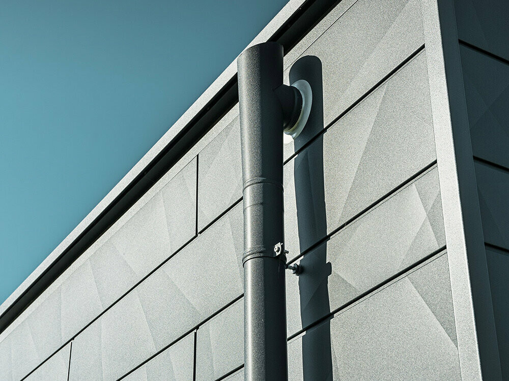 Tuyau de descente PREFA avec embranchement d'évacuation couleur P.10 anthracite sur une façade en Siding.X PREFA, elle aussi couleur P.10 anthracite