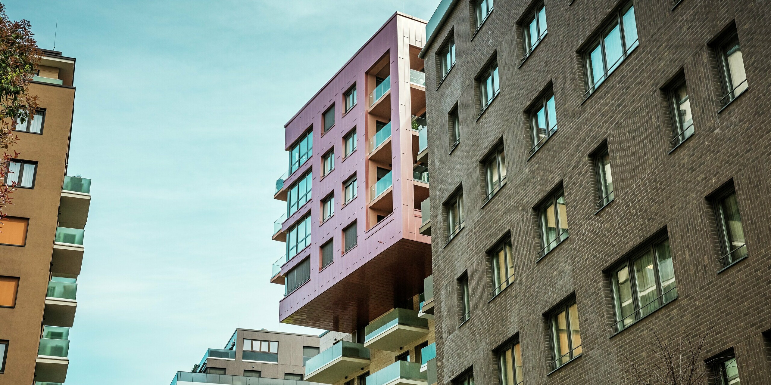 Vue de l'impressionnant bâtiment en porte-à-faux du projet Grand Corvin, dans le quartier Corvin de Budapest. Les étages supérieurs sont revêtus de panneaux de façade Siding PREFA, posés verticalement et d'une finition saumon métallisé particulière. La façade en aluminium robuste se détache nettement de l'architecture en briques environnante et souligne le caractère architectural moderne du quartier revitalisé.