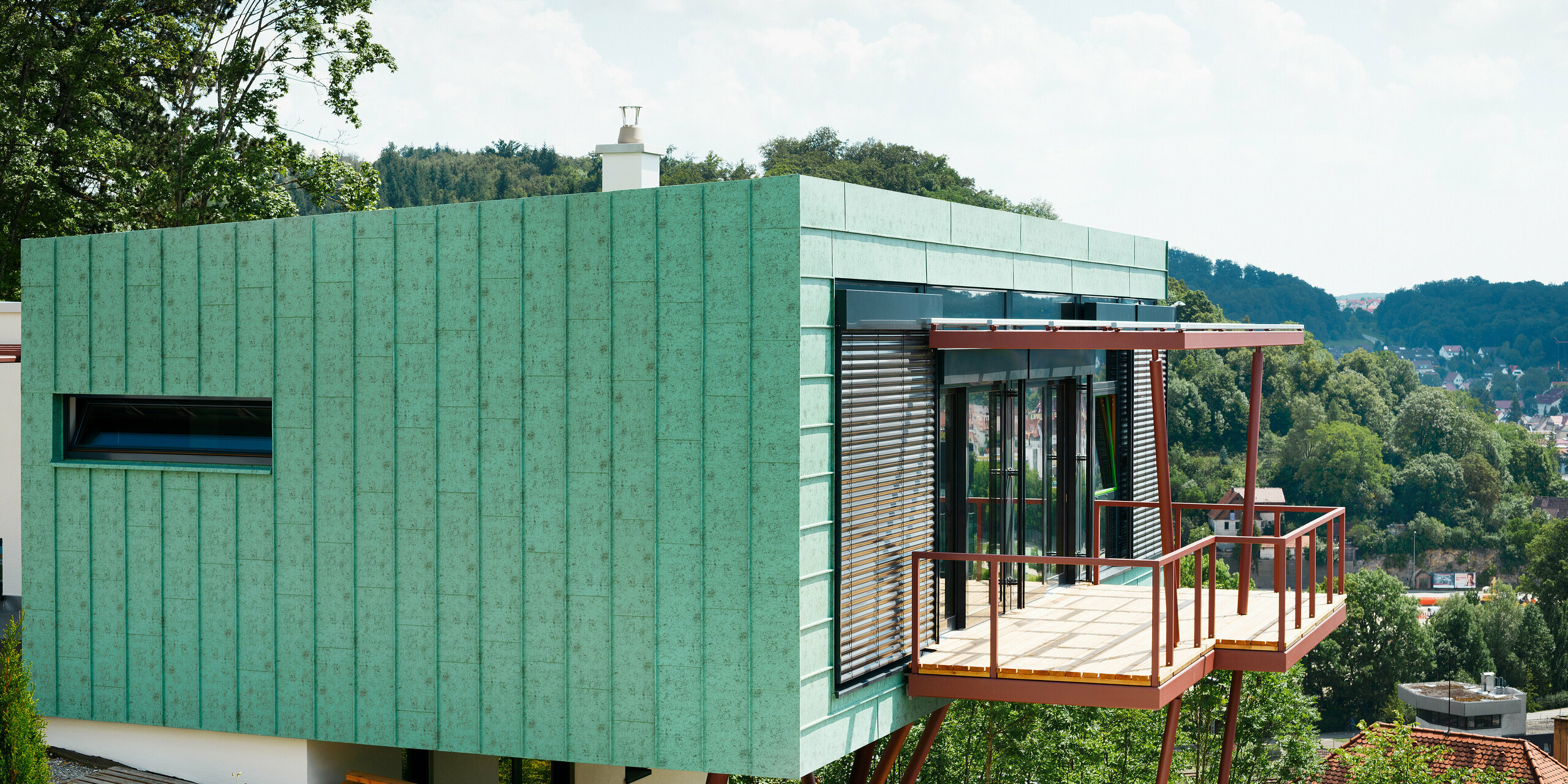 Das Heidenheimer Wohnhauses wird umhüllt von einer markanten PREFALZ-Fassade in Patina-Grün, die in der Sonne glänzt. Die perfekte Kombination aus Funktionalität und Design wird durch die widerstandsfähigen Eigenschaften der PREFALZ-Fassade verstärkt. Sie trotzt nicht nur dem Wetter, sondern garantiert auch eine lange Lebensdauer. Diese Fassade hebt die Schönheit und Beständigkeit des Gebäudes auf ein neues Niveau.