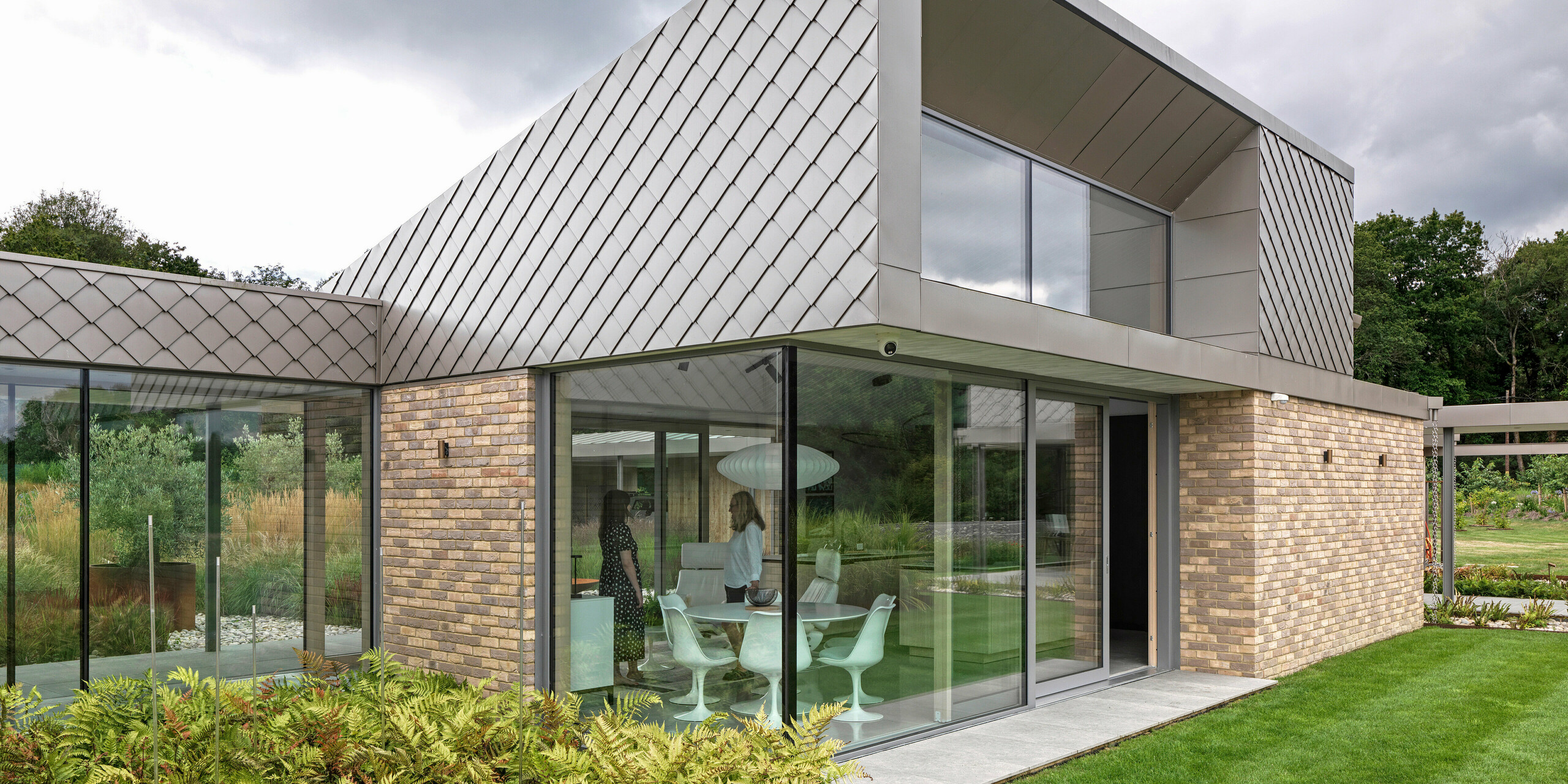 Un élément architectural remarquable d'un immeuble résidentiel du West Sussex, avec une façade moderne en losanges de façade PREFA 20 x 20 en P.10 bronze. Les toitures, recouvertes d'aluminium PREFALZ, aux lignes épurées, soulignent le caractère intemporel du projet. De généreuses façades vitrées créent des espaces de vie lumineux et relient visuellement le bâtiment au jardin soigné. Les produits PREFA de haute qualité offrent durabilité et un aspect uniforme avec un entretien minimal.
