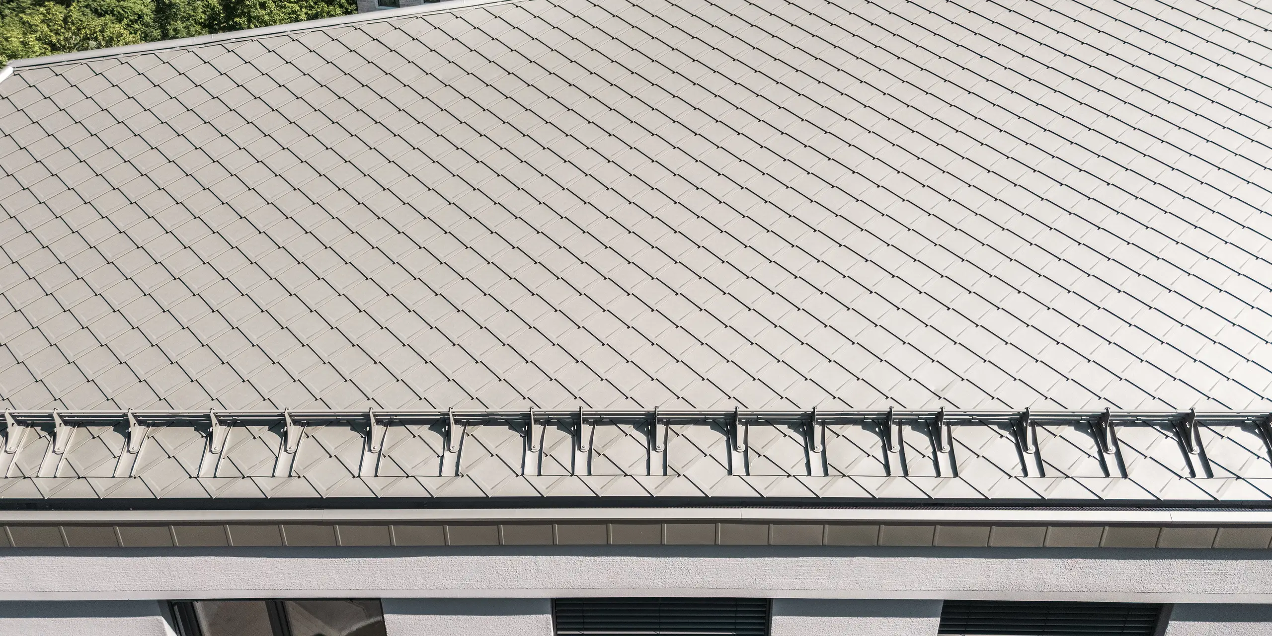 Die detailreiche Nahaufnahme des Daches der Sparkasse Blaubeuren zeigt die präzise Verlegung der PREFA Dachrauten 44 × 44 in Bronze. Das gleichmäßige Rautenmuster verleiht der großzügigen Dachfläche eine elegante, strukturierte Optik. Ein integriertes Schneefangsystem ergänzt die Dachgestaltung. Die leichten, langlebigen und witterungsbeständigen Aluminiumrauten überzeugen durch Ästhetik und Funktionalität.