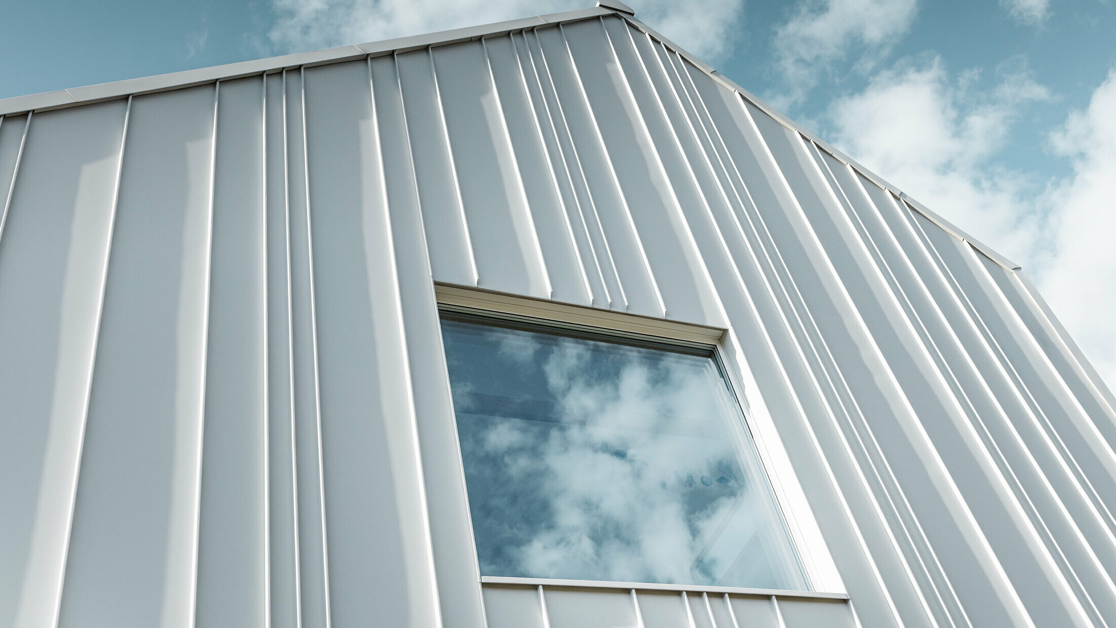 weißes PREFALZ als Winkelstehfalz an der Fassade mit unterschiedlichen Scharenbreiten und einem Fenster