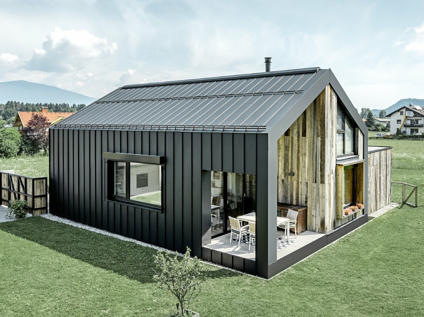 Maison individuelle avec toit à pignon ; la toiture et la façade sont recouvertes avec PREFALZ de PREFA en P.10 anthracite. Les bacs de la surface de toit se prolongent jusque sur la façade. Une partie de la façade est revêtue de bois patiné.