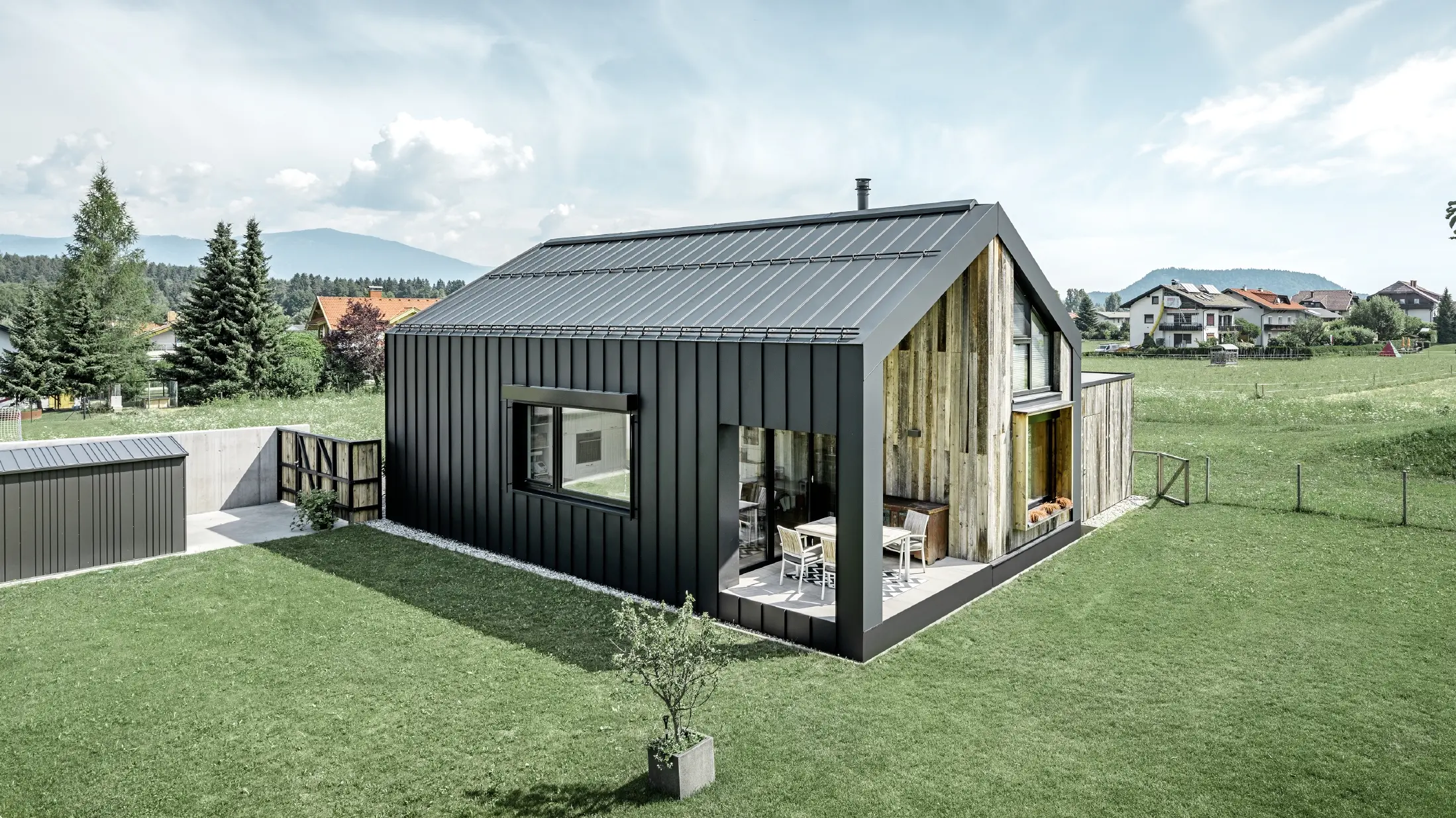 Eengezinswoning met zadeldak, dak- en gevelbedekking met PREFALZ van PREFA in P.10 antraciet. De panelen van het dak lopen door over de gevel. Een deel van de gevel is bekleed met verweerd hout.