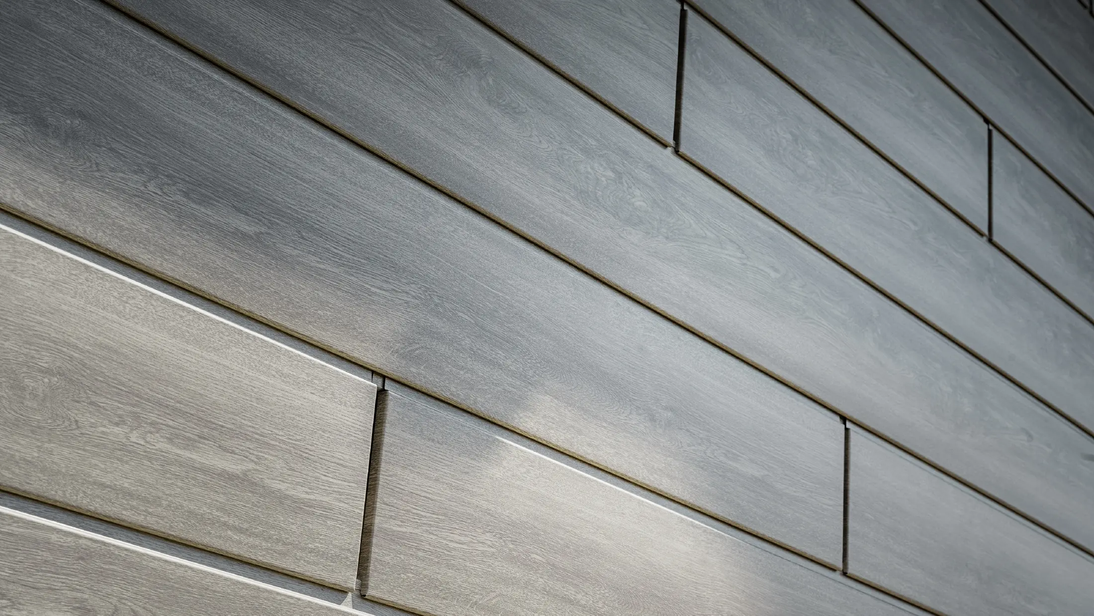 Close-up van de PREFA Sidings aluminium gevel, de aluminium panelen zijn horizontaal geplaatst en hebben een houtlook - grijs eiken.