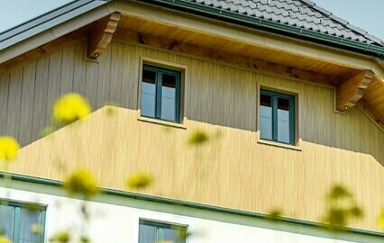 Topgevelbekleding met aluminium panelen van PREFA in hout-look (eiken naturel). De gevelbeplating is verwerkt in verticale richting, inclusief de bekleding van de onderkant van het dak.