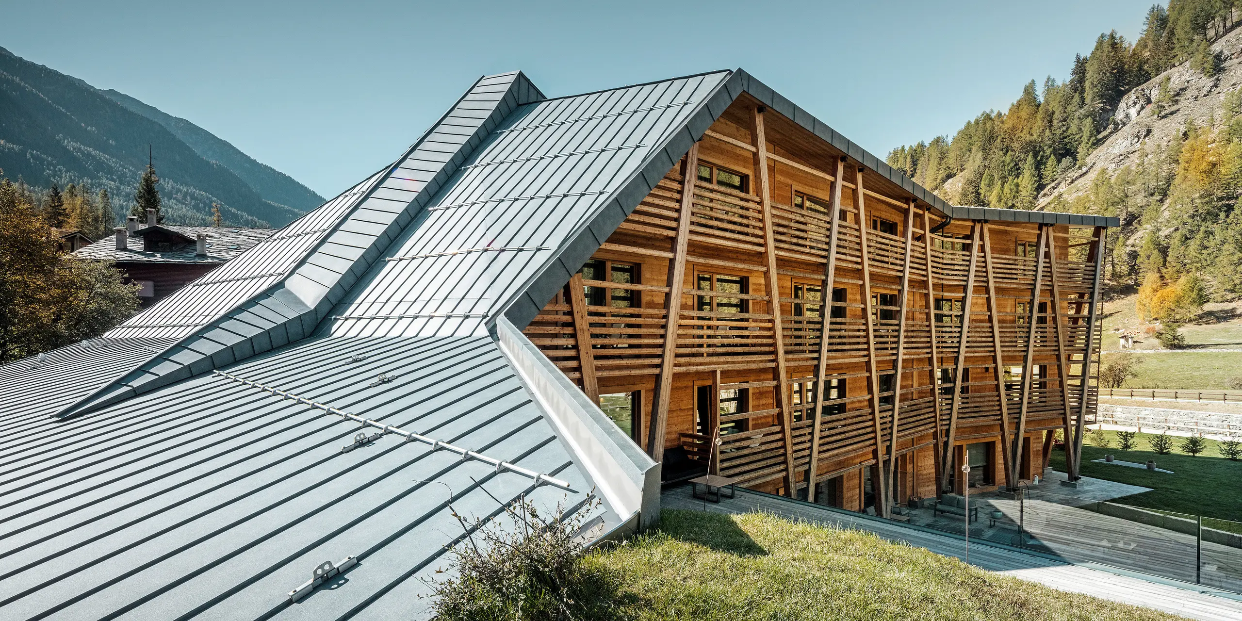 Das Hotel 'Au Charmant Petit Lac' in Champoluc zeigt eine einzigartige architektonische Harmonie, bei der das PREFALZ Dachsystem in P.10 Steingrau gekonnt mit der holzverkleideten Struktur des Gebäudes verschmilzt. Die dynamische Dachgestaltung mit ihren klaren Linien und Falzen fügt sich nahtlos in die umliegende Alpenlandschaft ein und bietet einen modernen Kontrast zur traditionellen Holzbauweise. Diese Kombination aus modernen und natürlichen Materialien spiegelt das Engagement des Hotels für umweltbewusstes Design und Nachhaltigkeit wider.