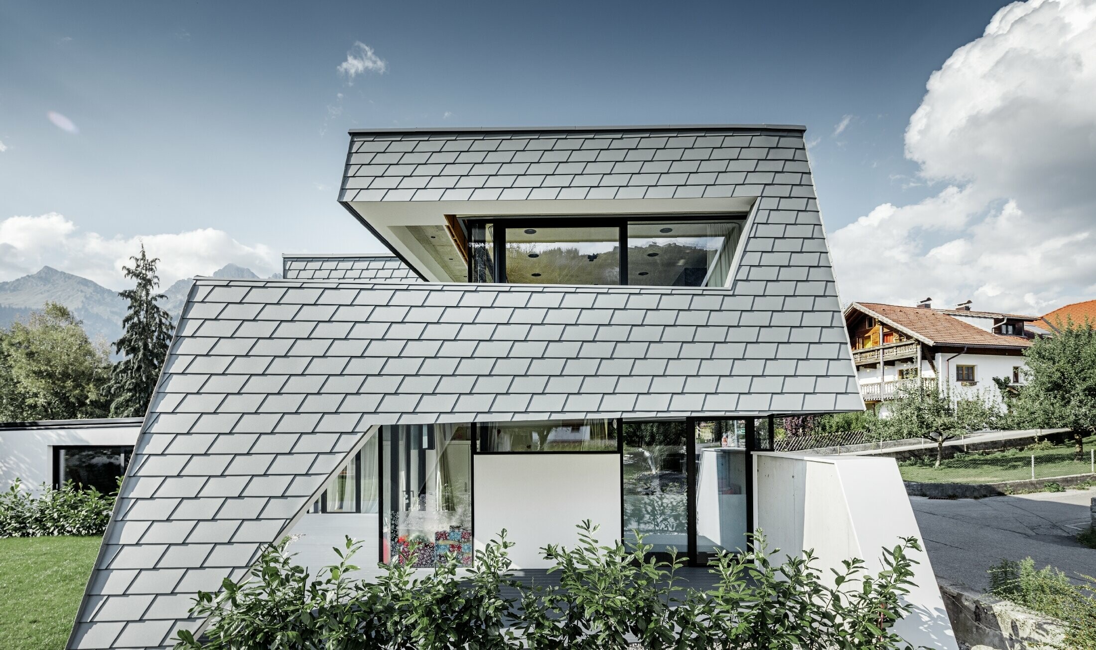 Moderne gezinswoning met plat dak, grote raamoppervlakken en aluminiumgevel met lichtgrijze schindels van PREFA
