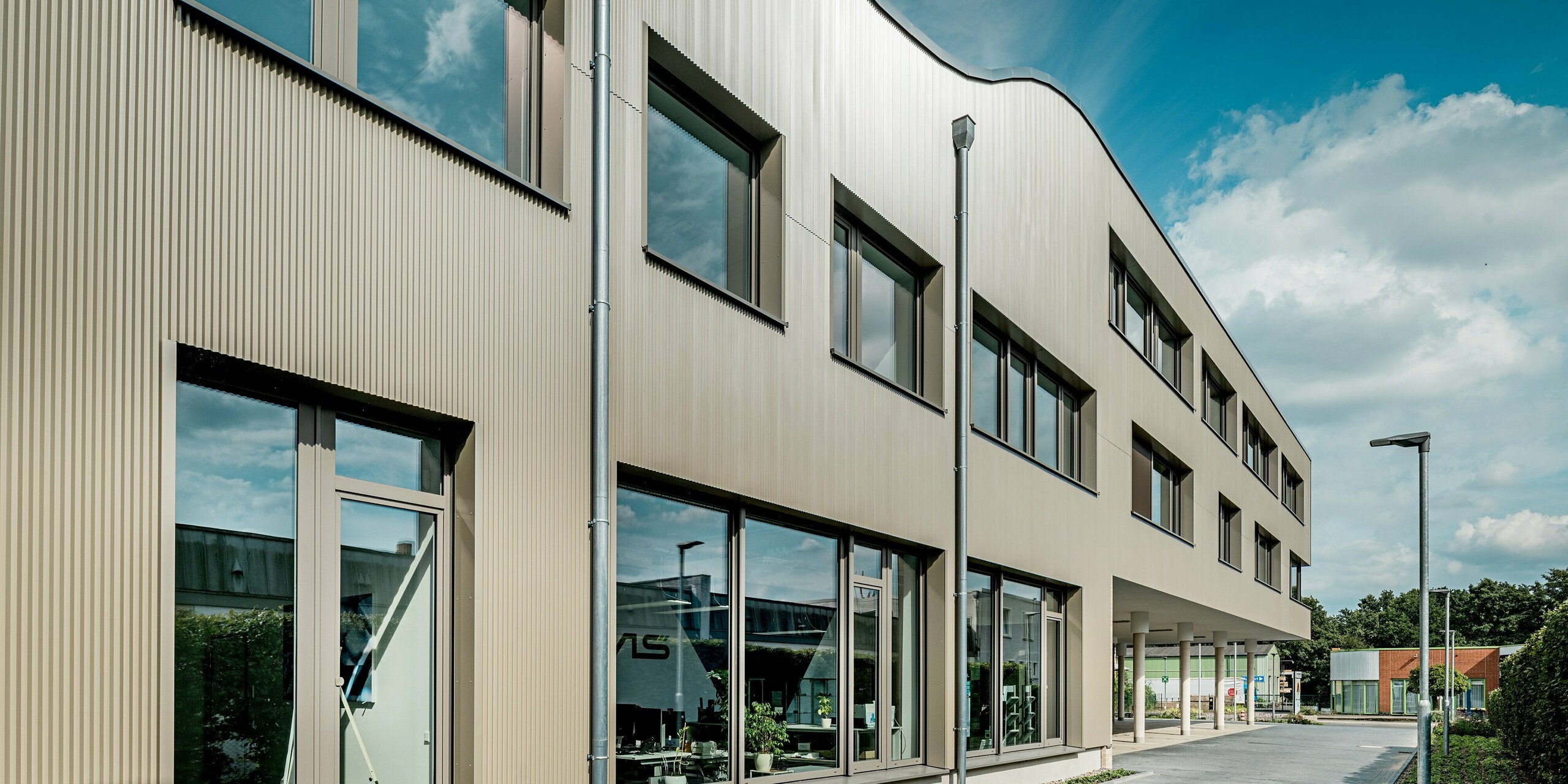 Das Bild zeigt das moderne Festo-Gebäude in Langenhagen, dessen prägnante Fassade mit PREFA Strangpressprofilen in Zackenform beeindruckt. Die Zacken verleihen der Fassade eine markante Textur und sorgen für eine einzigartige optische Wirkung. Die wellenartige Struktur des Gebäudes hebt sich eindrucksvoll vom klaren, geometrischen Design ab und fügt sich harmonisch in die Umgebung ein. Die große Glasfläche und die eleganten Aluminium Verbundplatten ergänzen das Fassadendesign perfekt und bieten eine moderne, zeitlose Ästhetik. Dank der langlebigen und pflegeleichten PREFA Materialien ist die Fassade optimal vor Witterungseinflüssen geschützt und bleibt über Jahre hinweg in einwandfreiem Zustand.