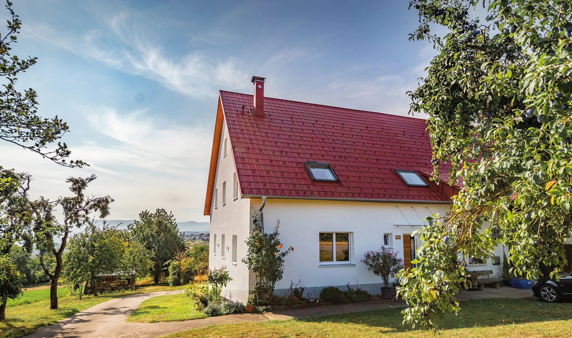 Maisonnette romantique à la campagne avec de nombreux arbres et arbustes. Recouverte avec une toiture PREFA couleur rouge oxyde.