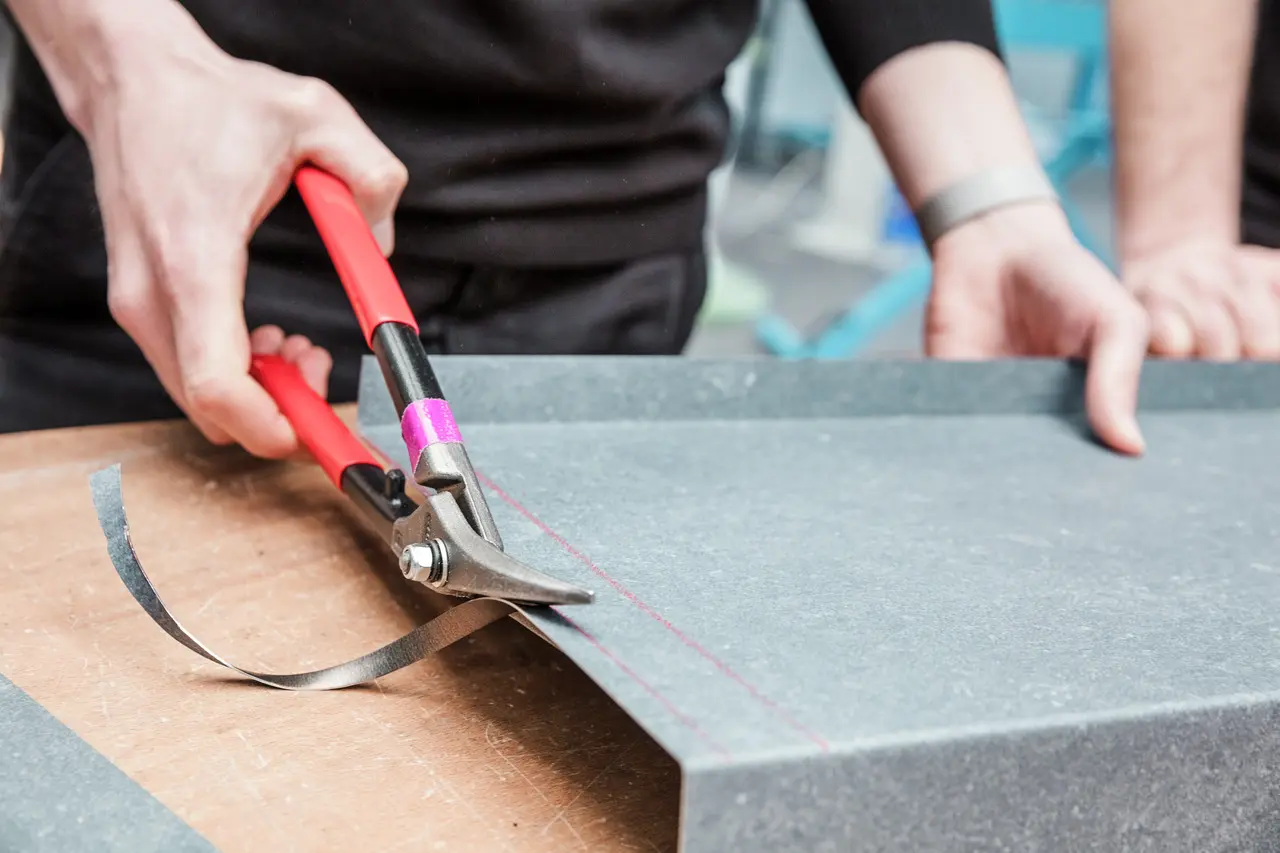 Ein Teilnehmer der PREFA Academy schneidet mit einer Blechschere präzise eine Aluminiumplatte entlang einer markierten Linie. Die Szene zeigt praktische Schulungsmaßnahmen, bei denen handwerkliche Fähigkeiten im Umgang mit Aluminium vermittelt werden.