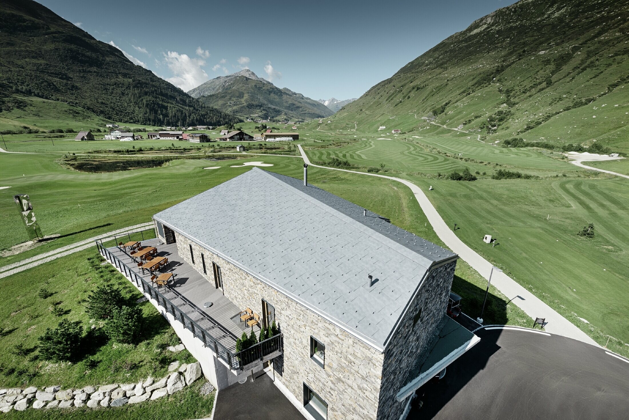 Club-house moderne du parcours de golf d’Andermatt en Suisse — Façade en pierre et panneaux de toiture FX.12 PREFA en aluminium de couleur gris pierre