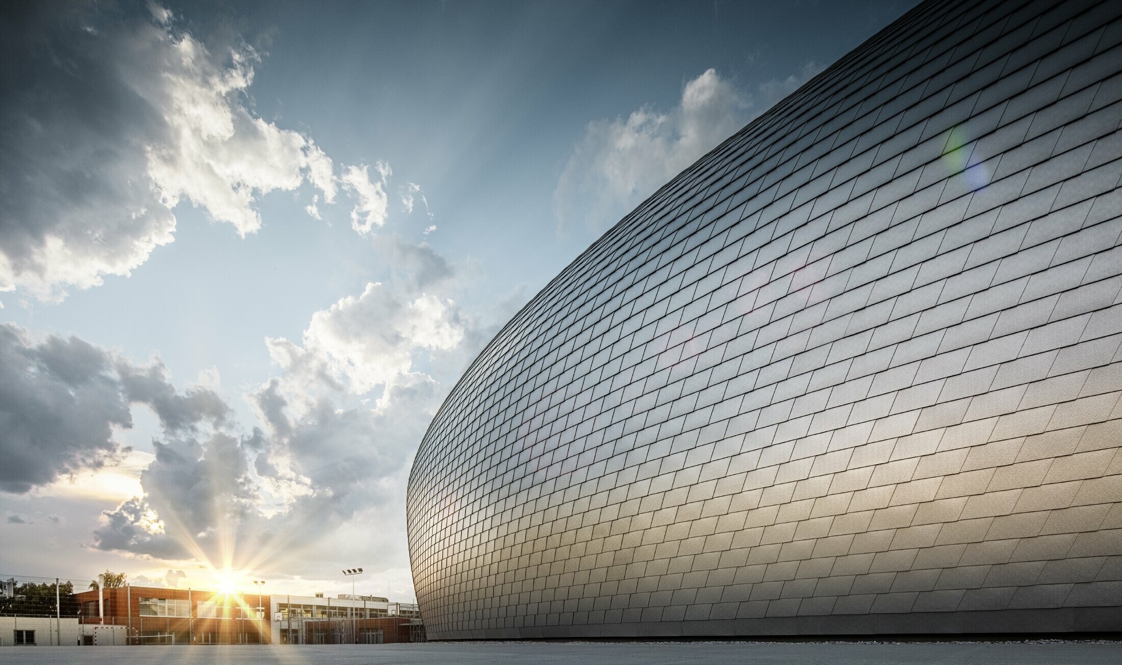 Sporthal in Tsjechië in de vorm van een ufo bekleed met de PREFA gevelschindel in naturel blank bij zonsopgang.