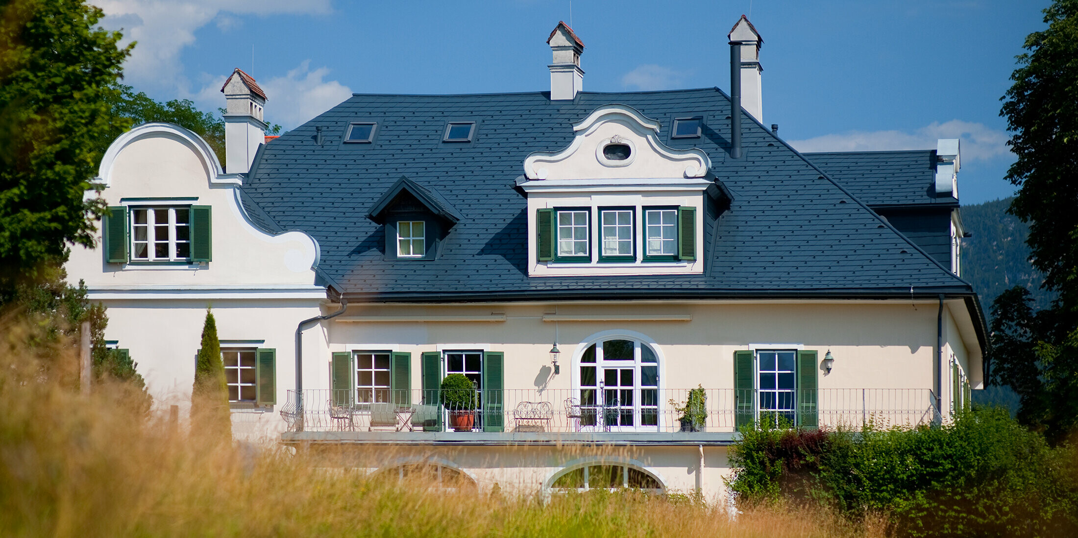 Blick aus der Ferne auf eine Villa in Bad Aussee, Österreich. Das Dach der Villa wurde mit robusten PREFA Dachschindeln in der Farbe P.10 Anthrazit verkleidet.