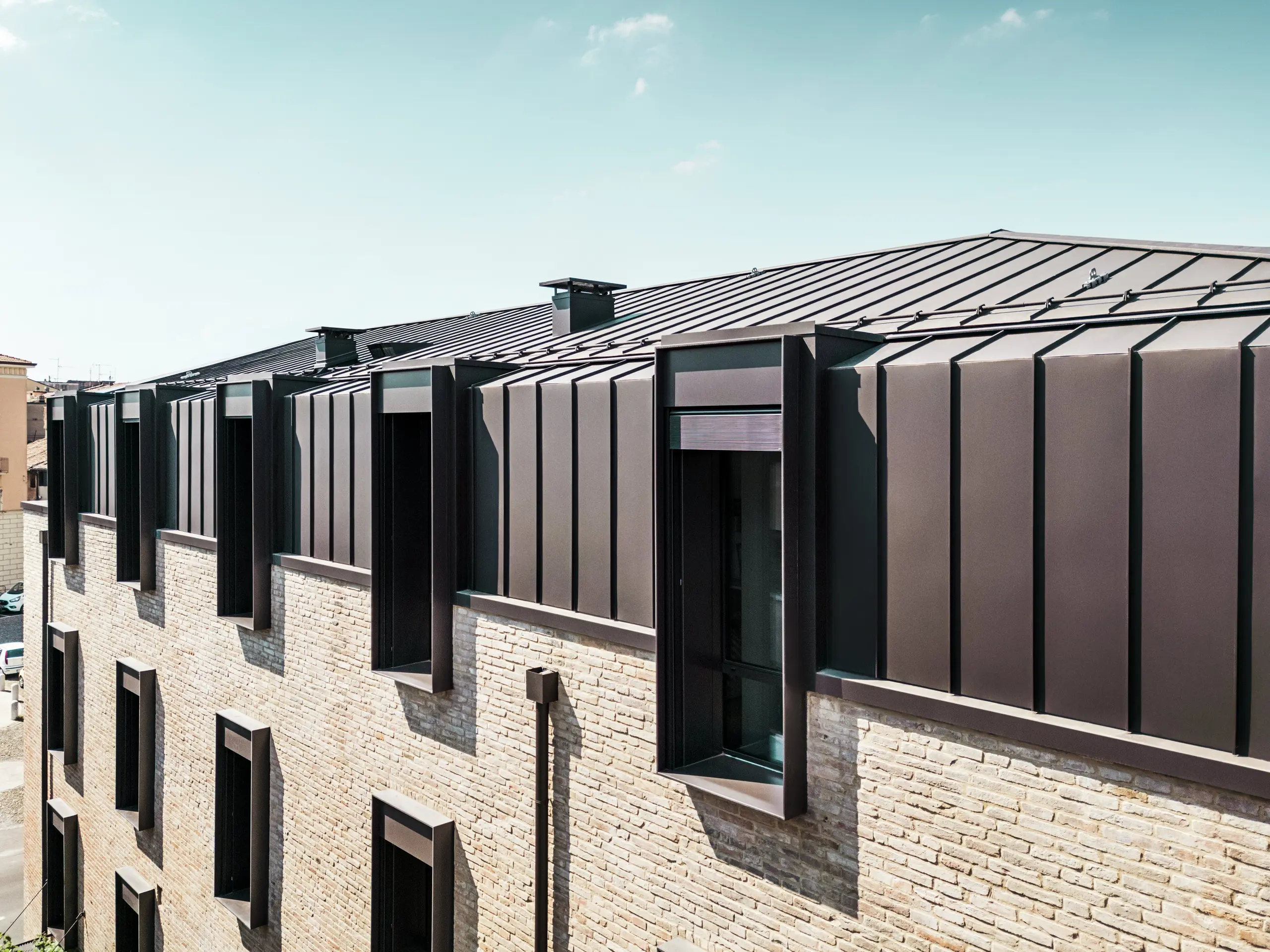 Moderne Dach- und Fassadengestaltung eines Backsteinhauses in Italien mit PREFALZ Aluminiumdach in der Farbe P.10 Nussbraun und markanten Fenstergauben