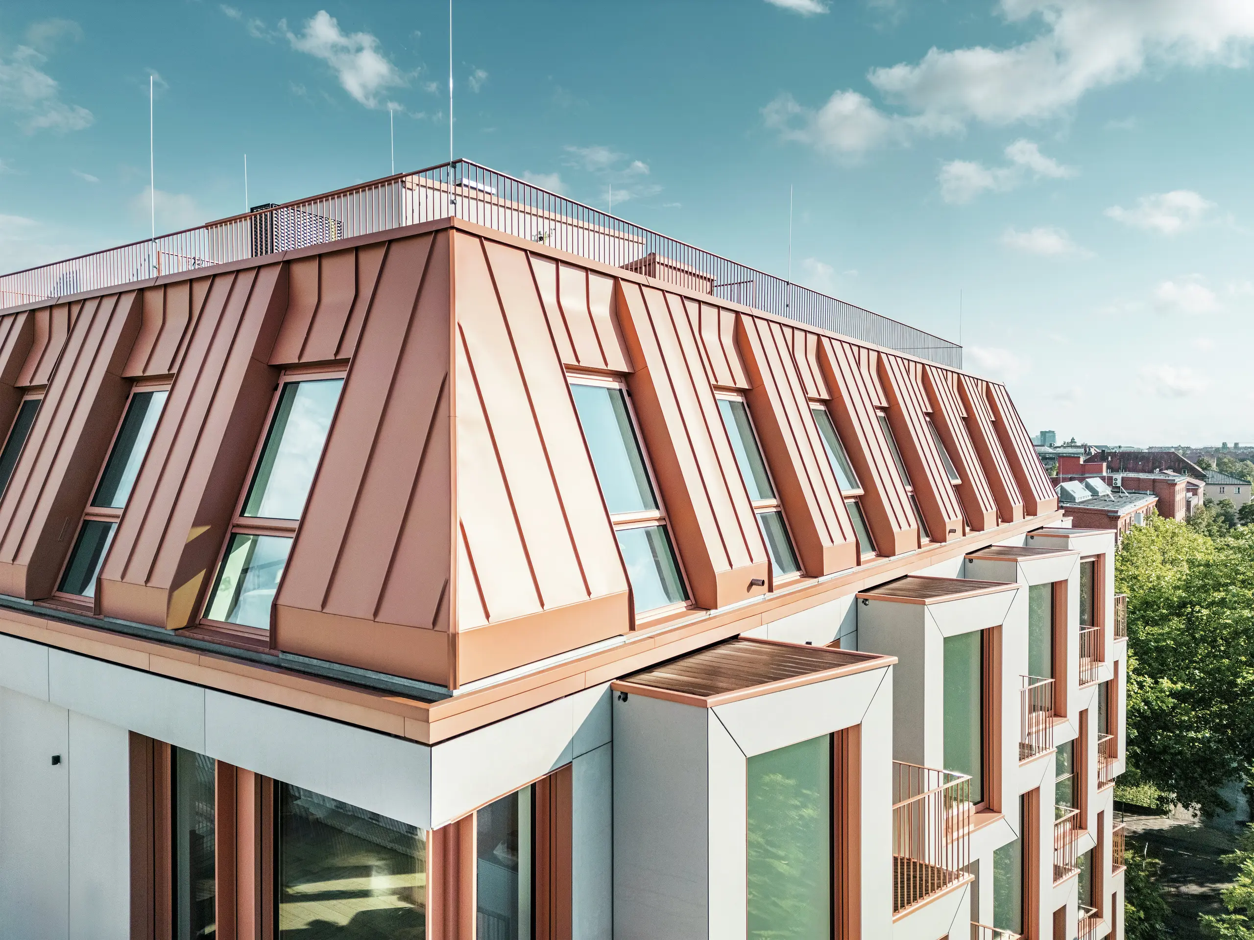 Vue détaillée de la remarquable couverture PREFALZ de l'immeuble résidentiel Van B à Munich. Le toit en aluminium de couleur assortie impressionne par sa finition de haute qualité, sa durabilité extrême et sa résistance aux intempéries. Les fenêtres inclinées et les éléments de façade clairement structurés complètent le concept de design innovant. Idéal pour l'architecture moderne, où fonctionnalité et esthétique vont de pair dans l'habitat urbain. Au bas de l'image, vous pouvez voir les rangées de baies vitrées.