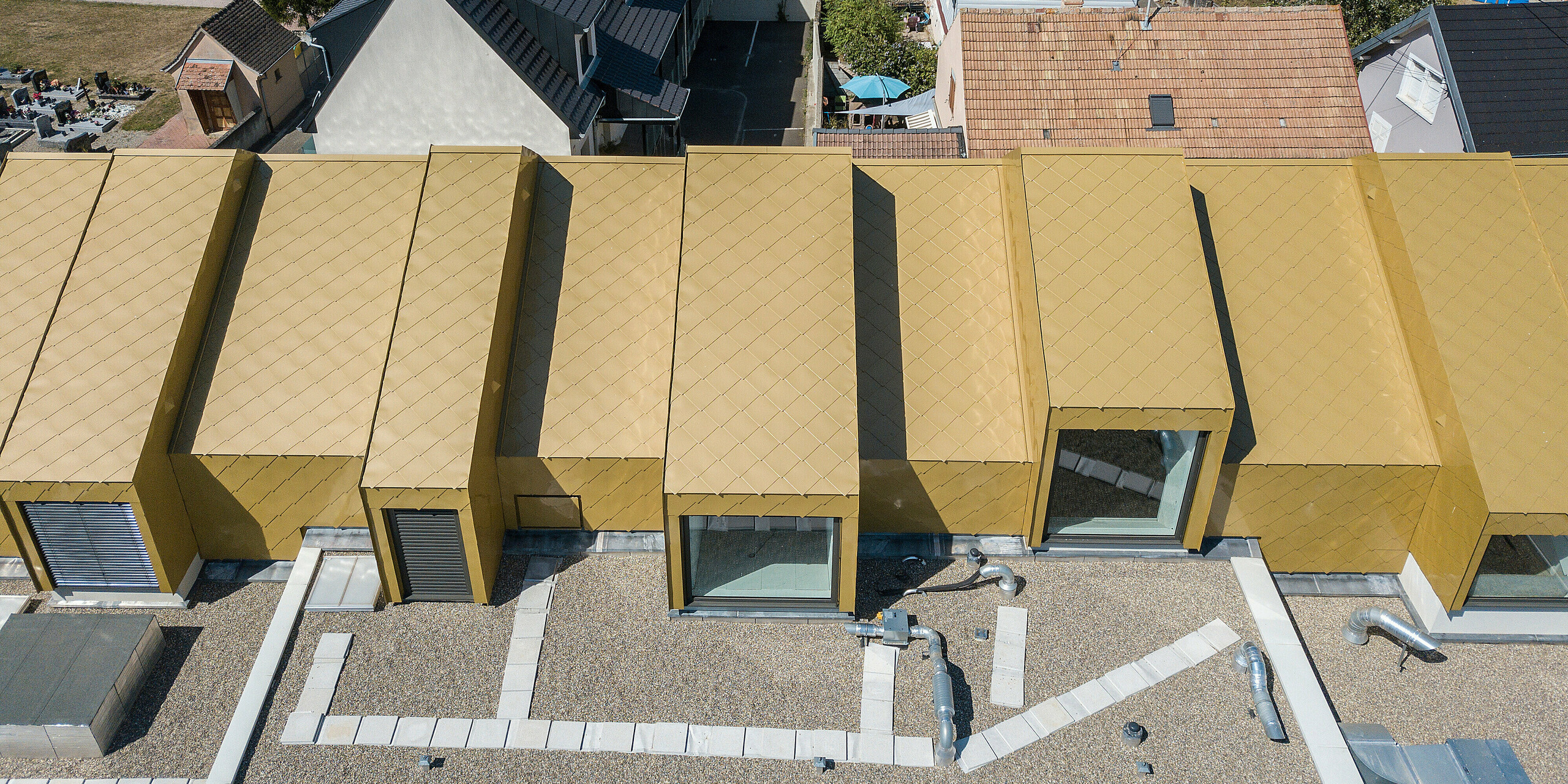 Vogelperspektive auf das goldene Dach des Gemeinde- und Kulturzentrums Fessenheim in Frankreich. Für das Renovierungsprojekt wurden PREFA Dach- und Wandrauten 44 × 44 in Sparkling Gold eingesetzt.