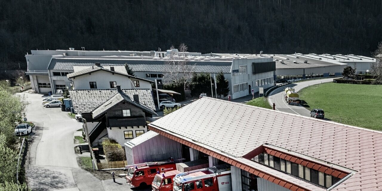 Vue aérienne de la caserne de sapeurs pompiers de l’entreprise à Marktl/Lilienfeld. La toiture et la façade de la partie gauche du bâtiment ont été entièrement habillées avec la tuile 44 couleur rouge oxyde. La partie droite est recouverte d’une enveloppe en aluminium réalisée avec Prefalz couleur argent métallisé.